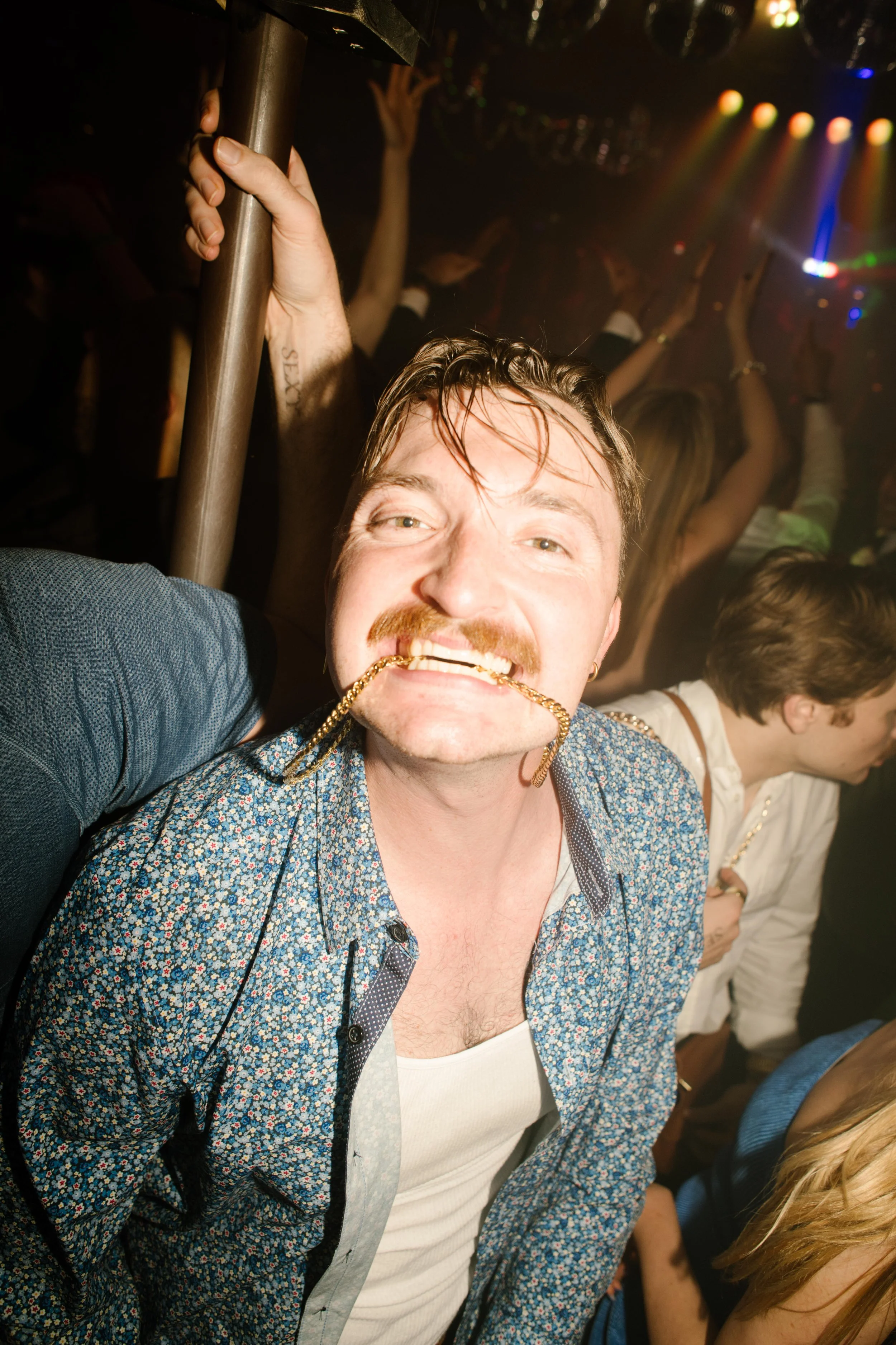Wedding guest joking with a gold chain in his mouth on a crowded dance floor during wedding after parties.