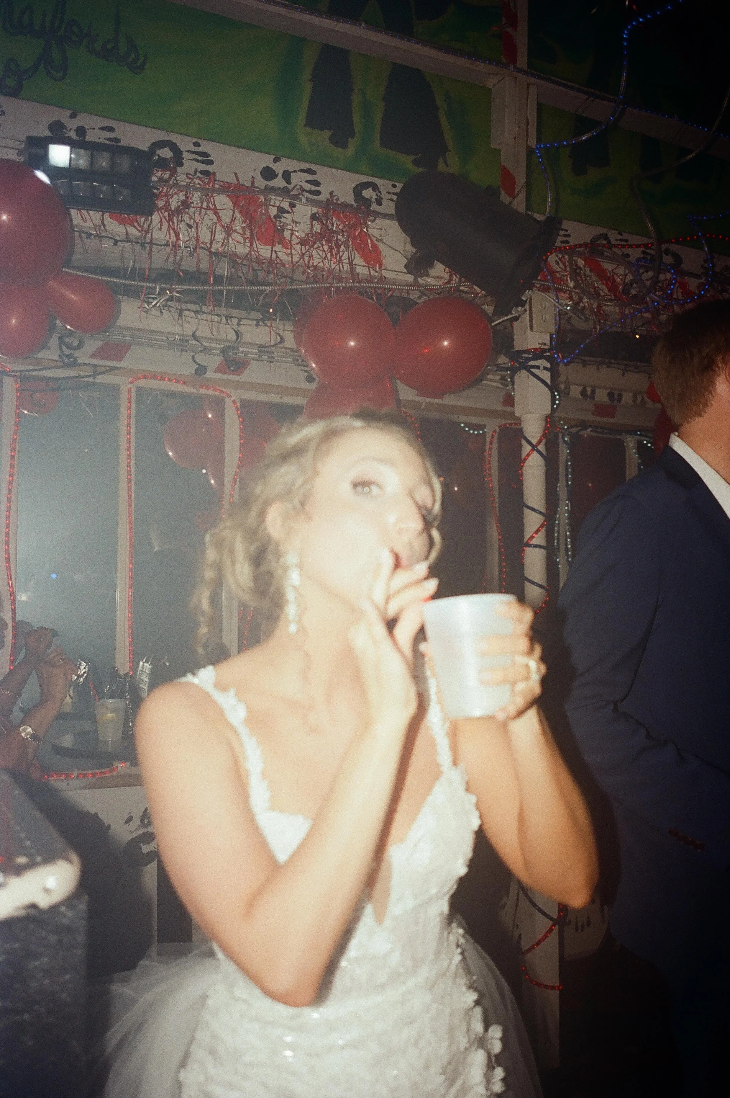 Bride sipping a drink inside a neon-lit nightclub during her wedding after party celebration.