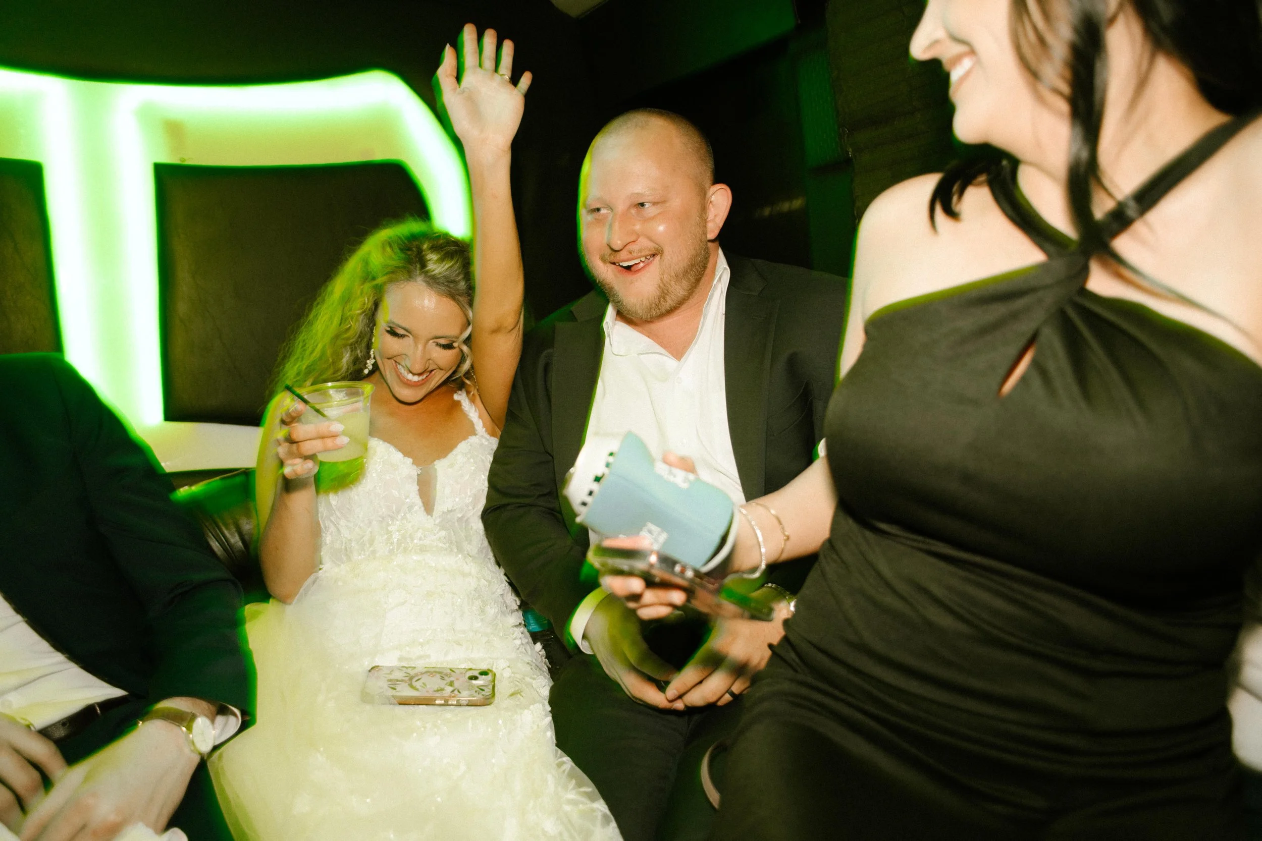 Bride celebrating with friends in a limo with drinks and neon lights after their wedding reception.