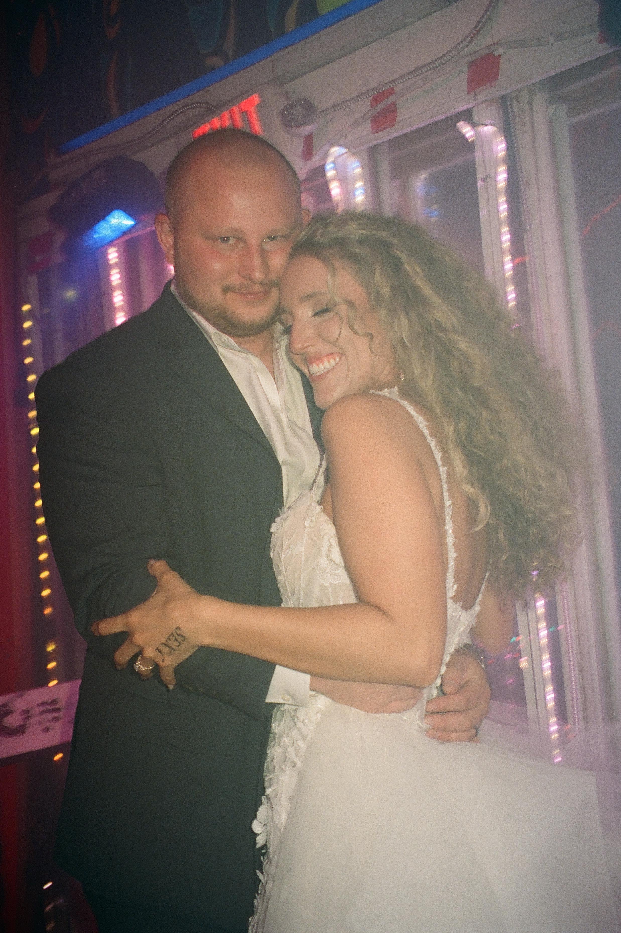 Bride and groom hugging outside a neon-lit nightclub during their wedding after party.