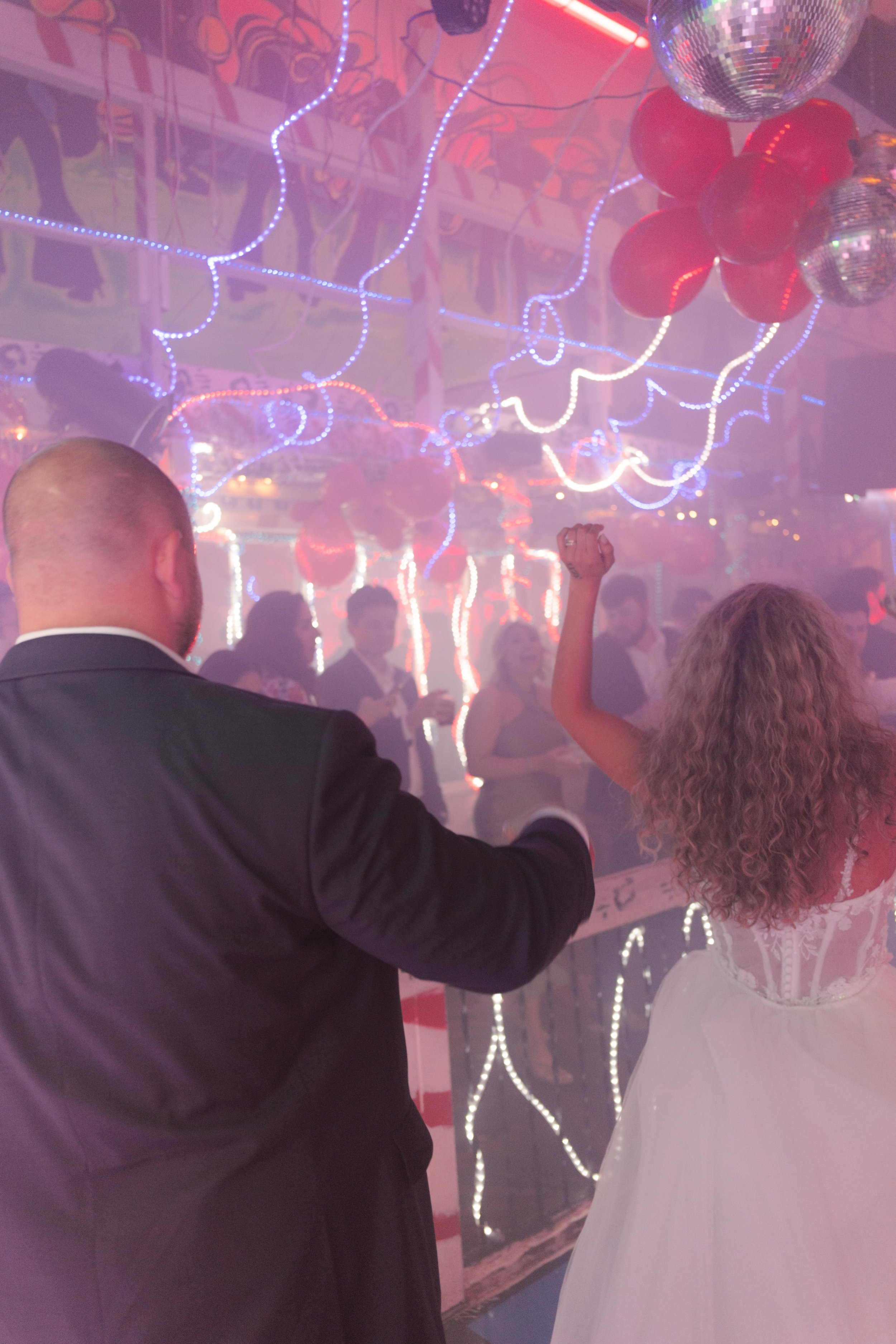 Newlyweds walking onto a neon-lit dance floor together as wedding after parties begin.