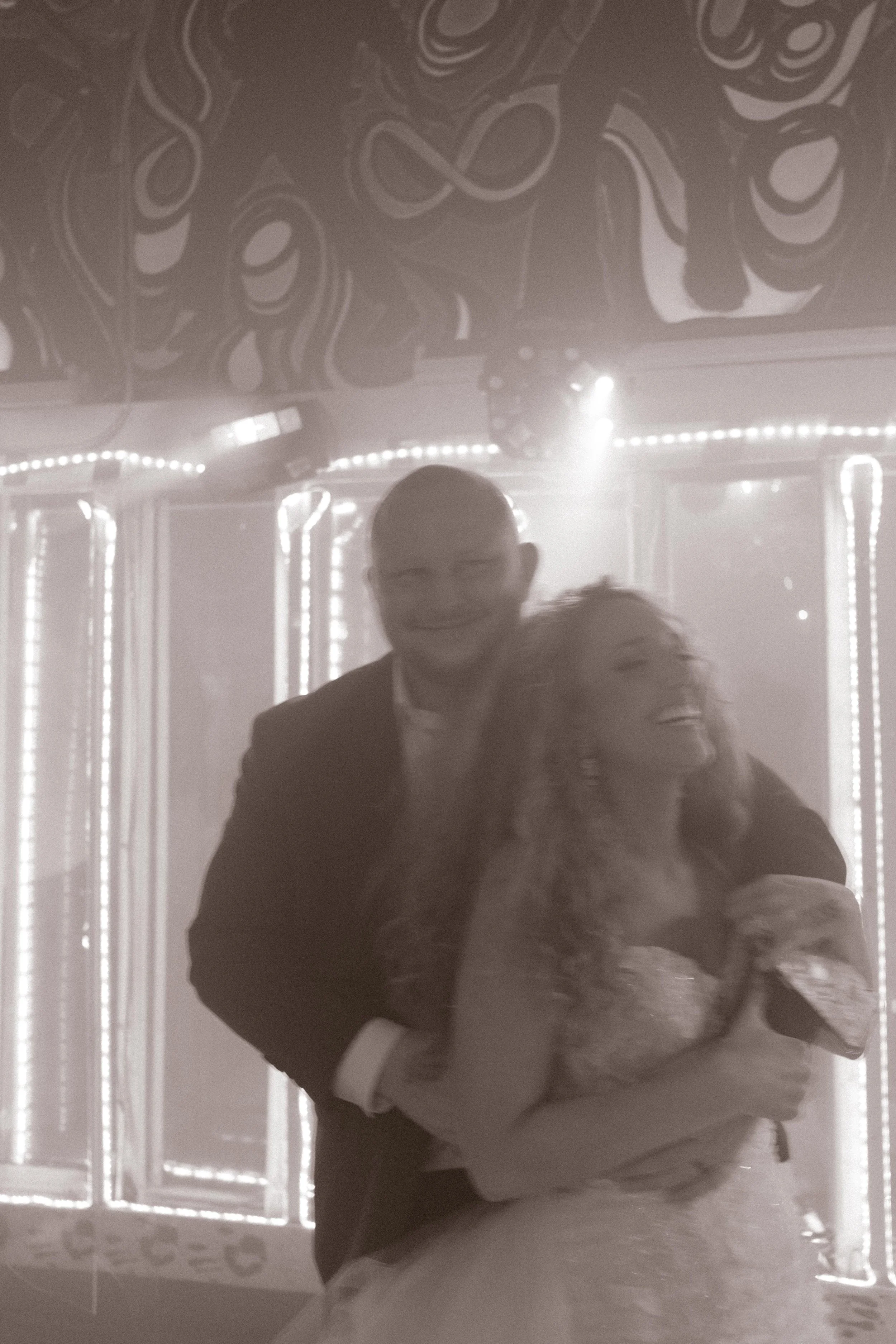 Bride laughing in the groom’s arms on a colorful dance floor during wedding after parties.