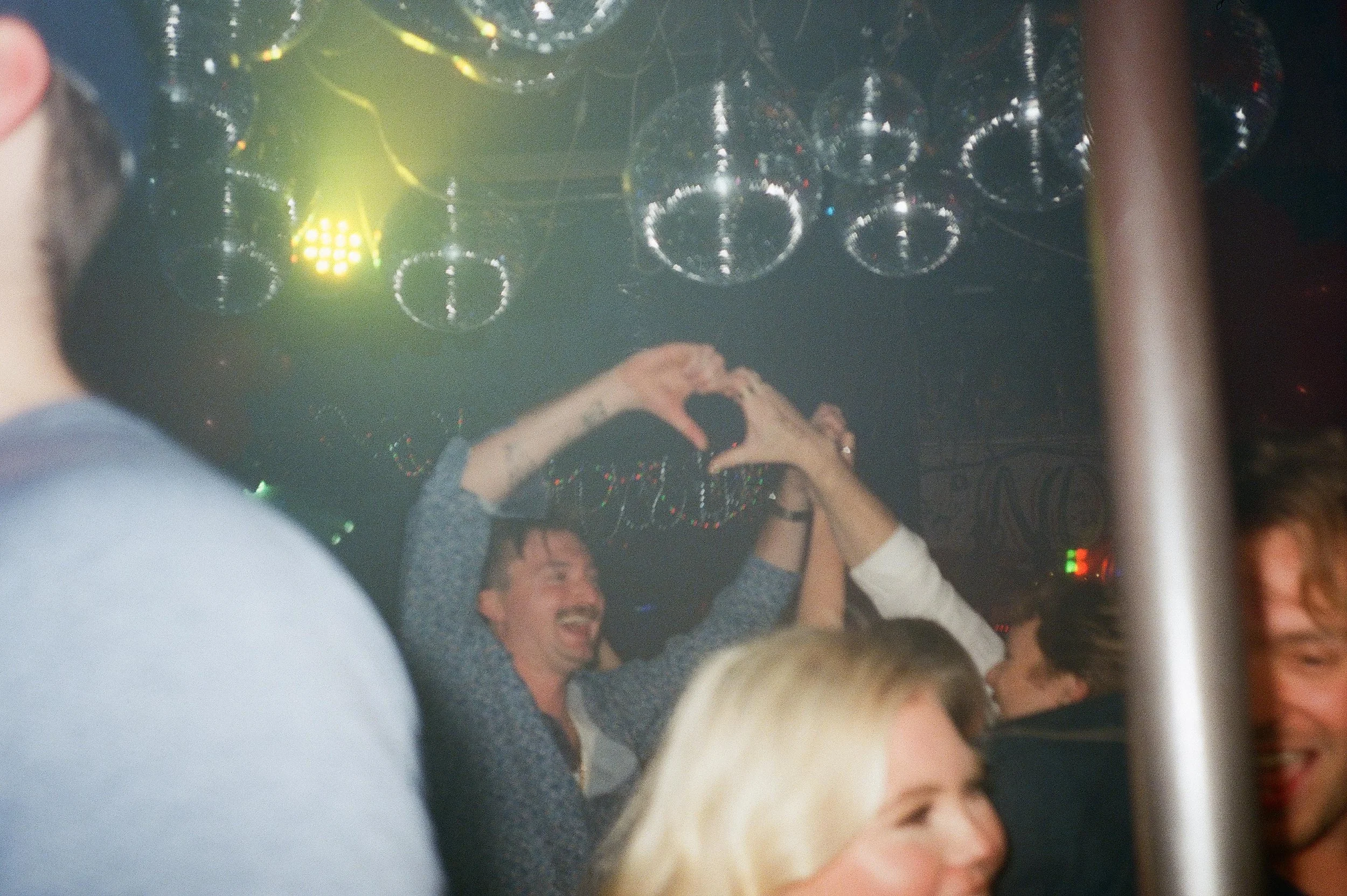 Wedding guests forming a heart with their hands under disco balls during wedding after parties.