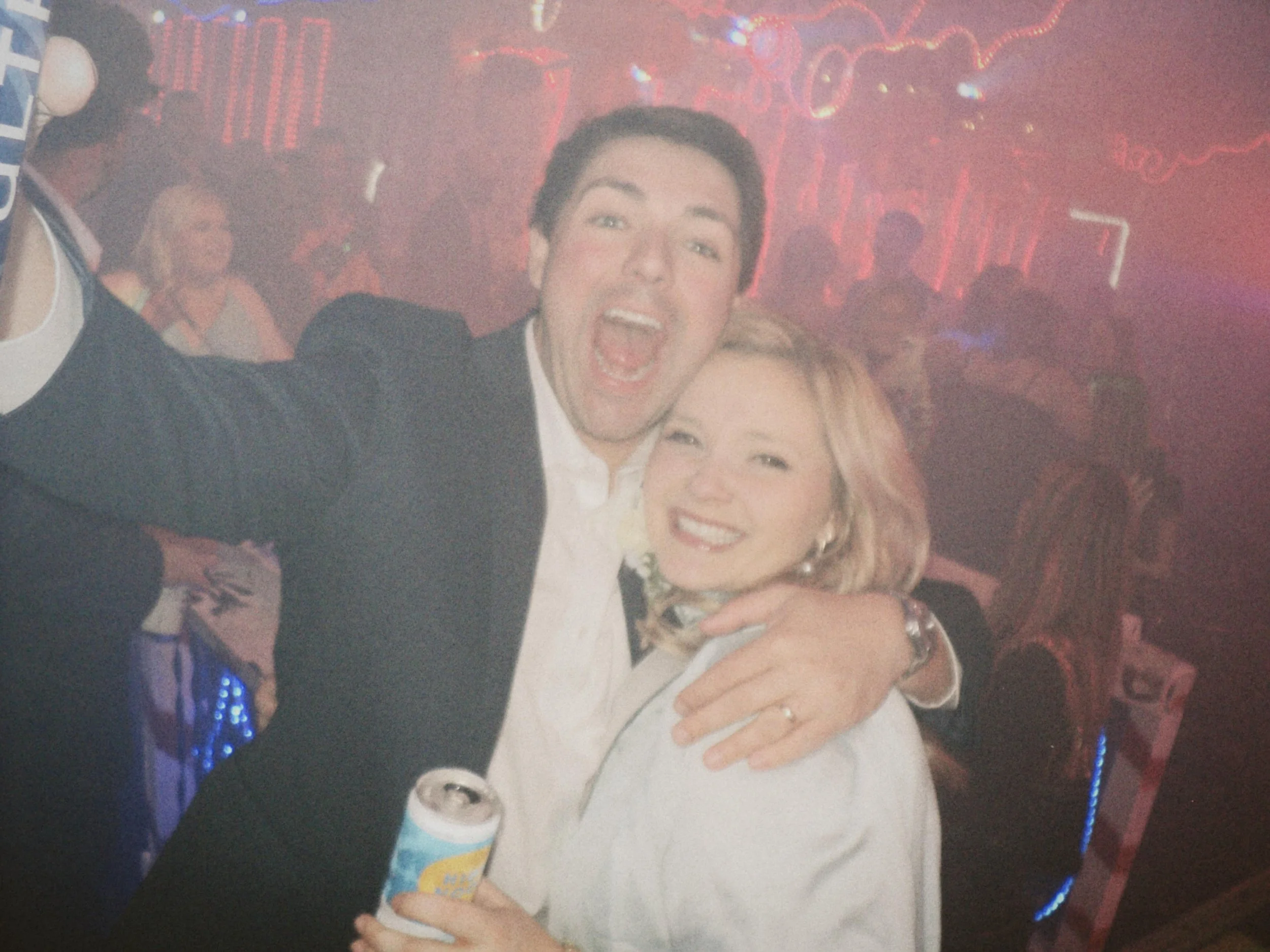 Two guests pose for a blurry, joy-filled snapshot on the dance floor, arms wrapped around each other and drinks in hand at the wedding after party.