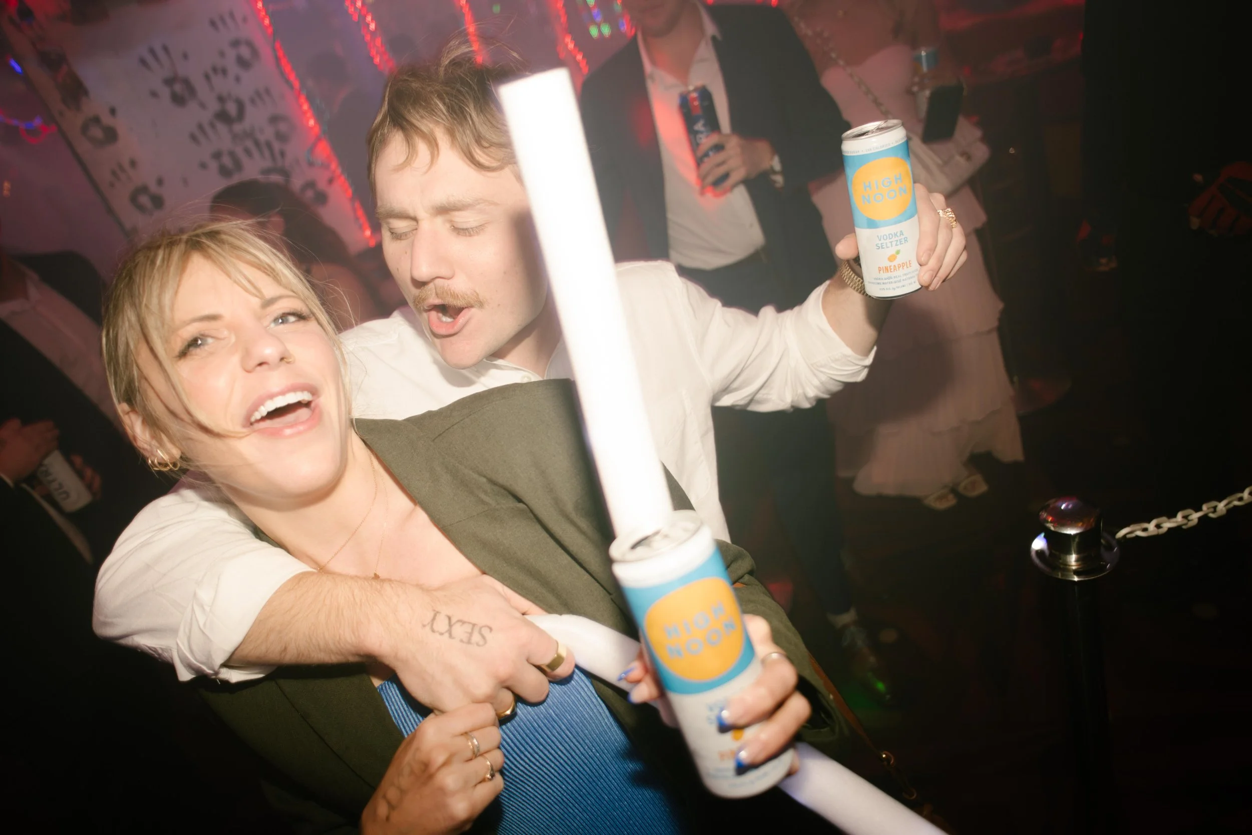 Guests laughing and holding drinks while dancing together at a crowded wedding after party.