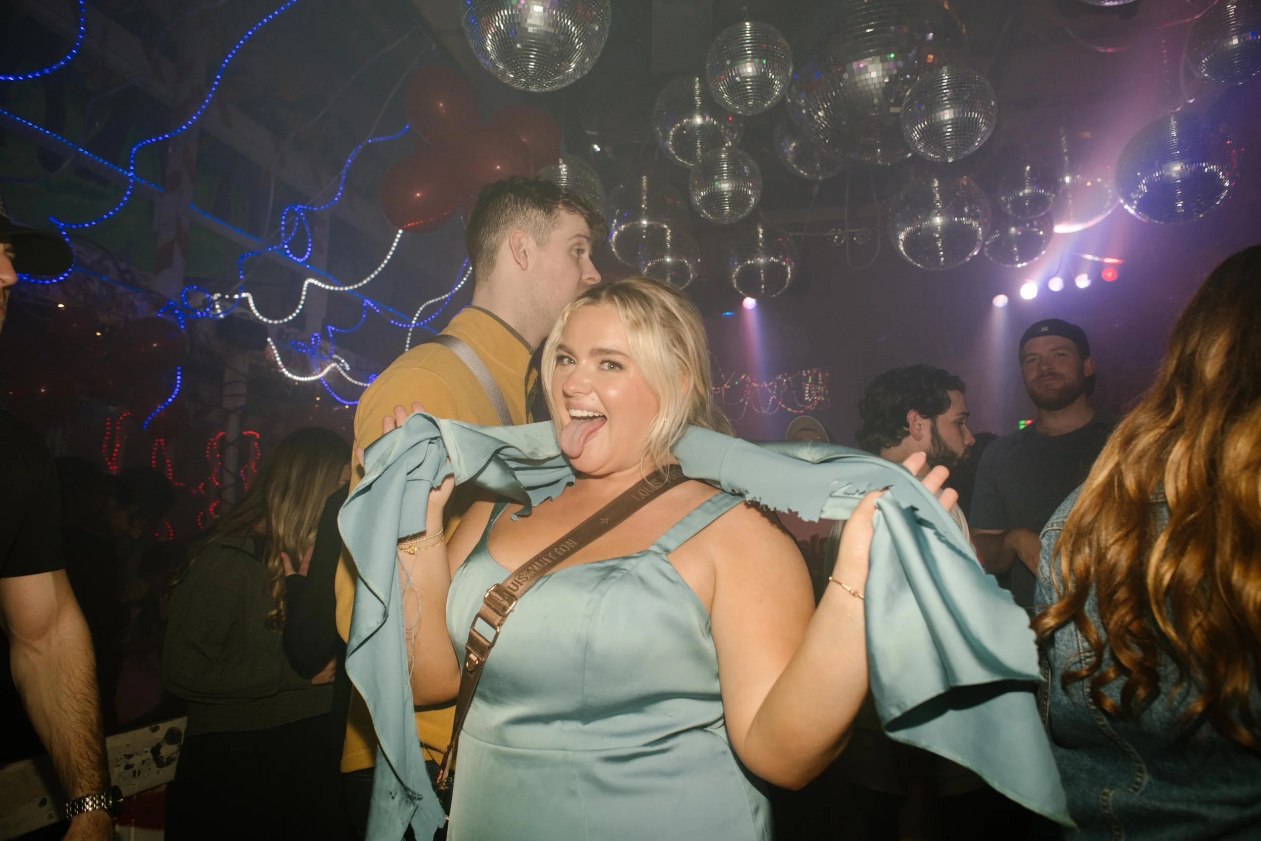 Wedding guest dancing under disco balls and neon lights during wedding after parties.