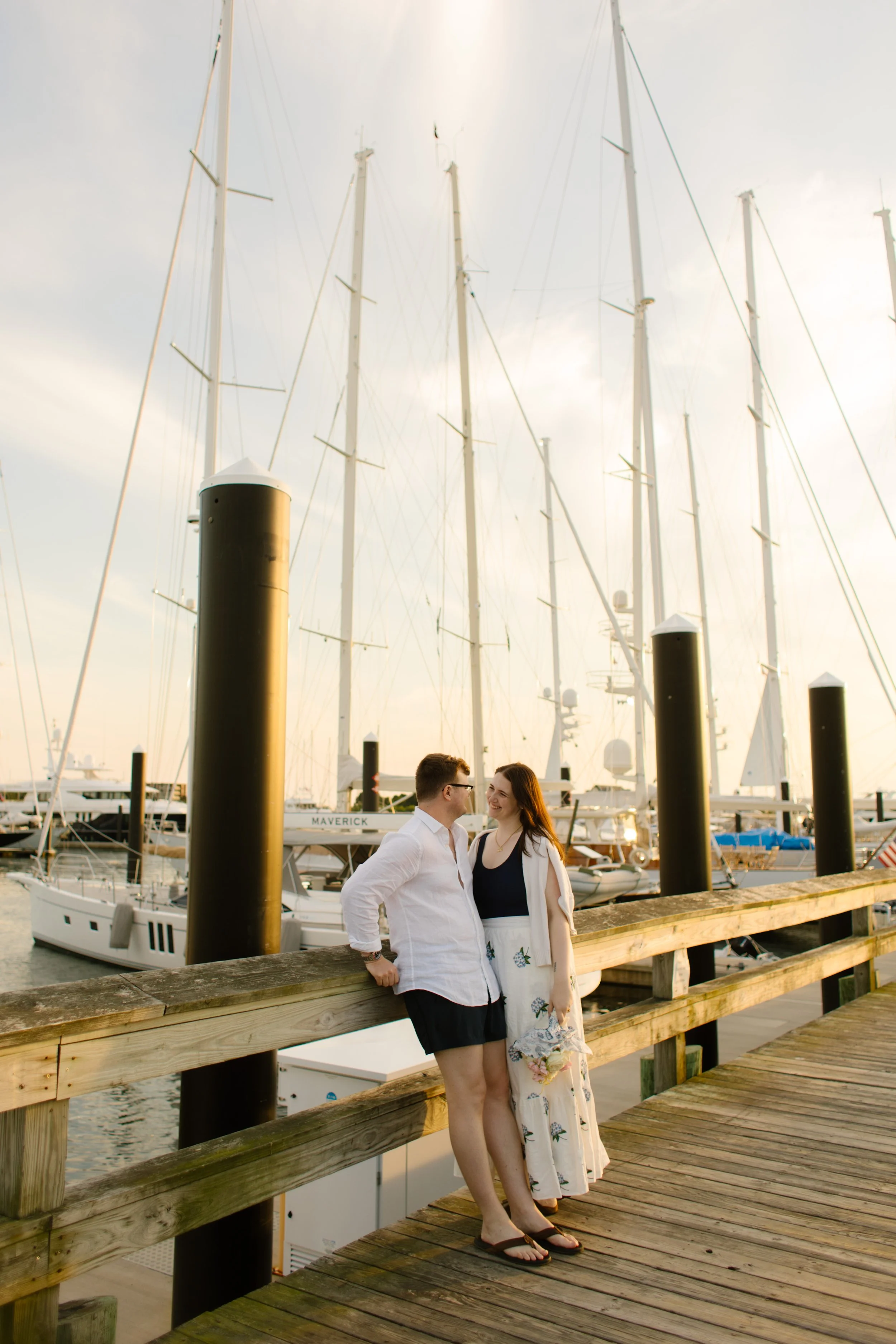 Couple leaning on harbor dock railing at sunset during Newport Rhode Island engagement photos