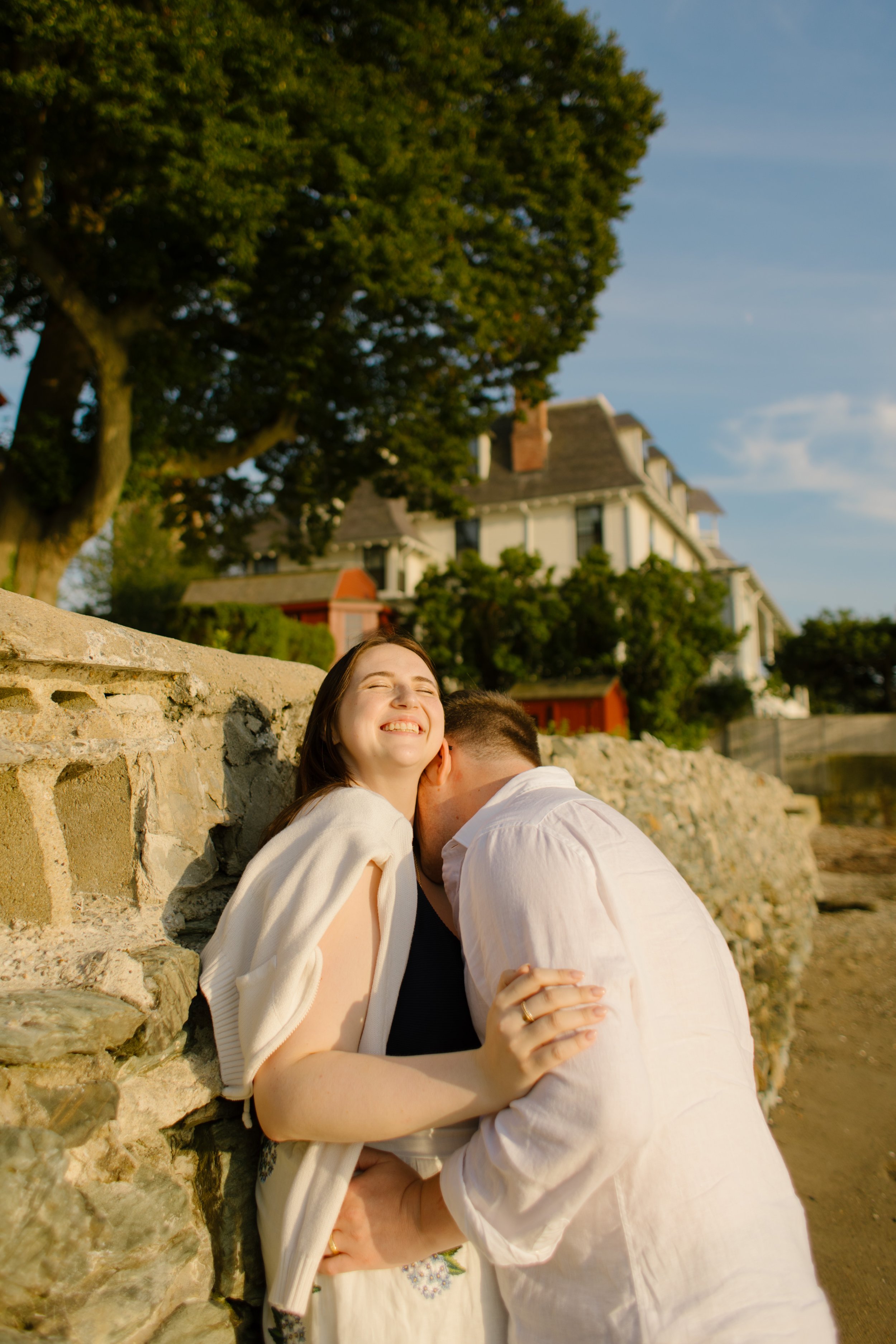 Playful candid moment of couple laughing by stone wall during Newport Rhode Island engagement photos