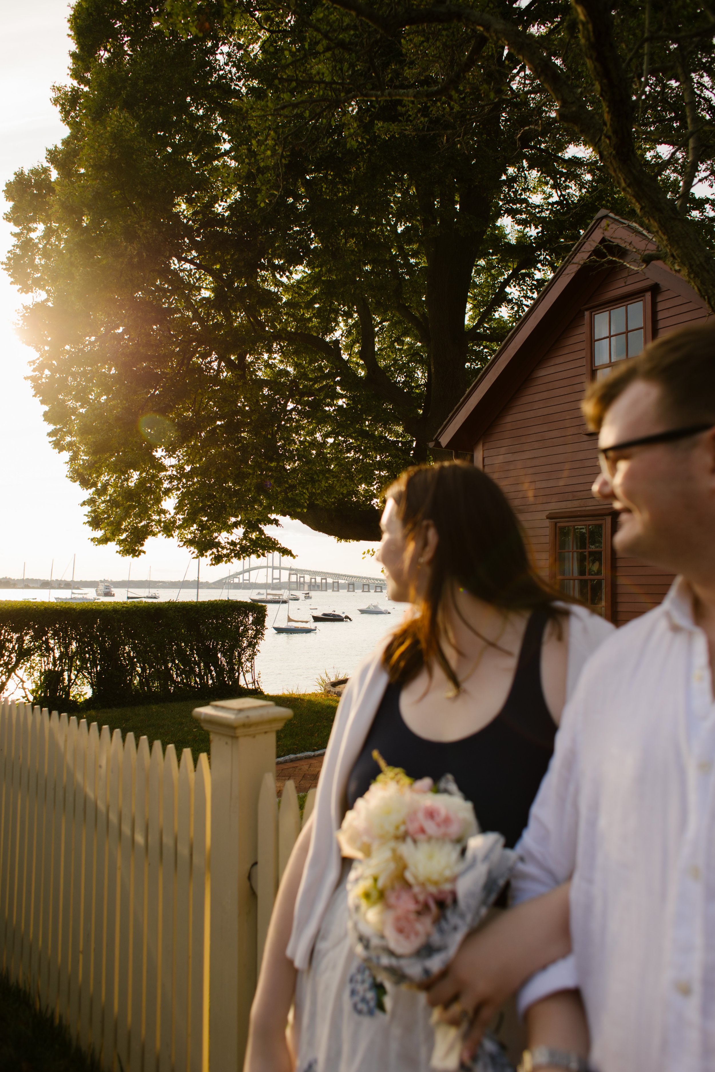 Couple walking beside harbor and picket fence at sunset during Newport Rhode Island engagement photos
