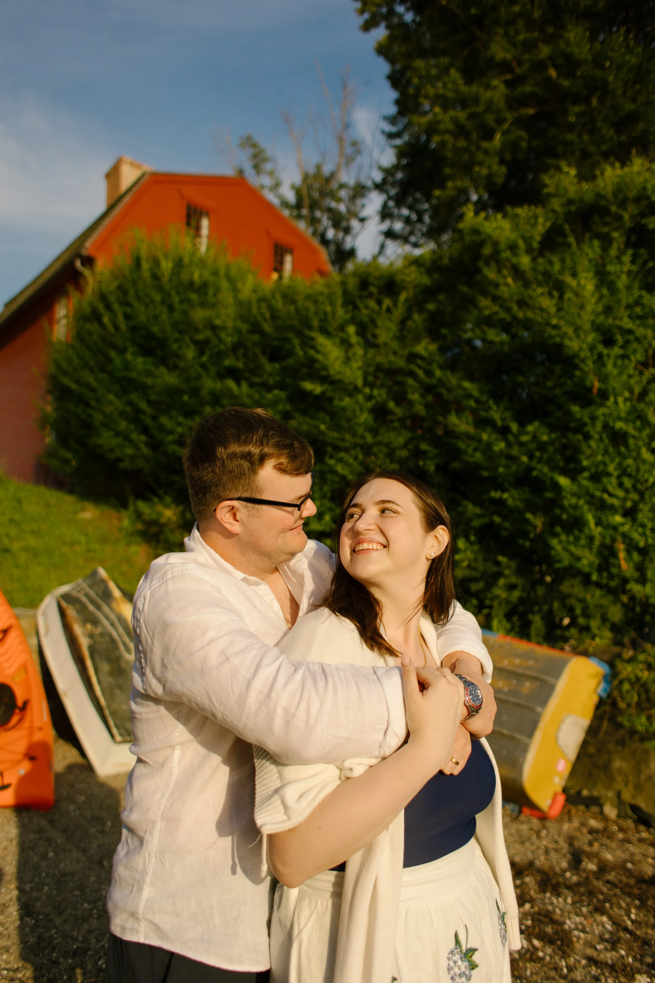 Couple embracing beside colorful boats on Newport shoreline during Newport Rhode Island engagement photos