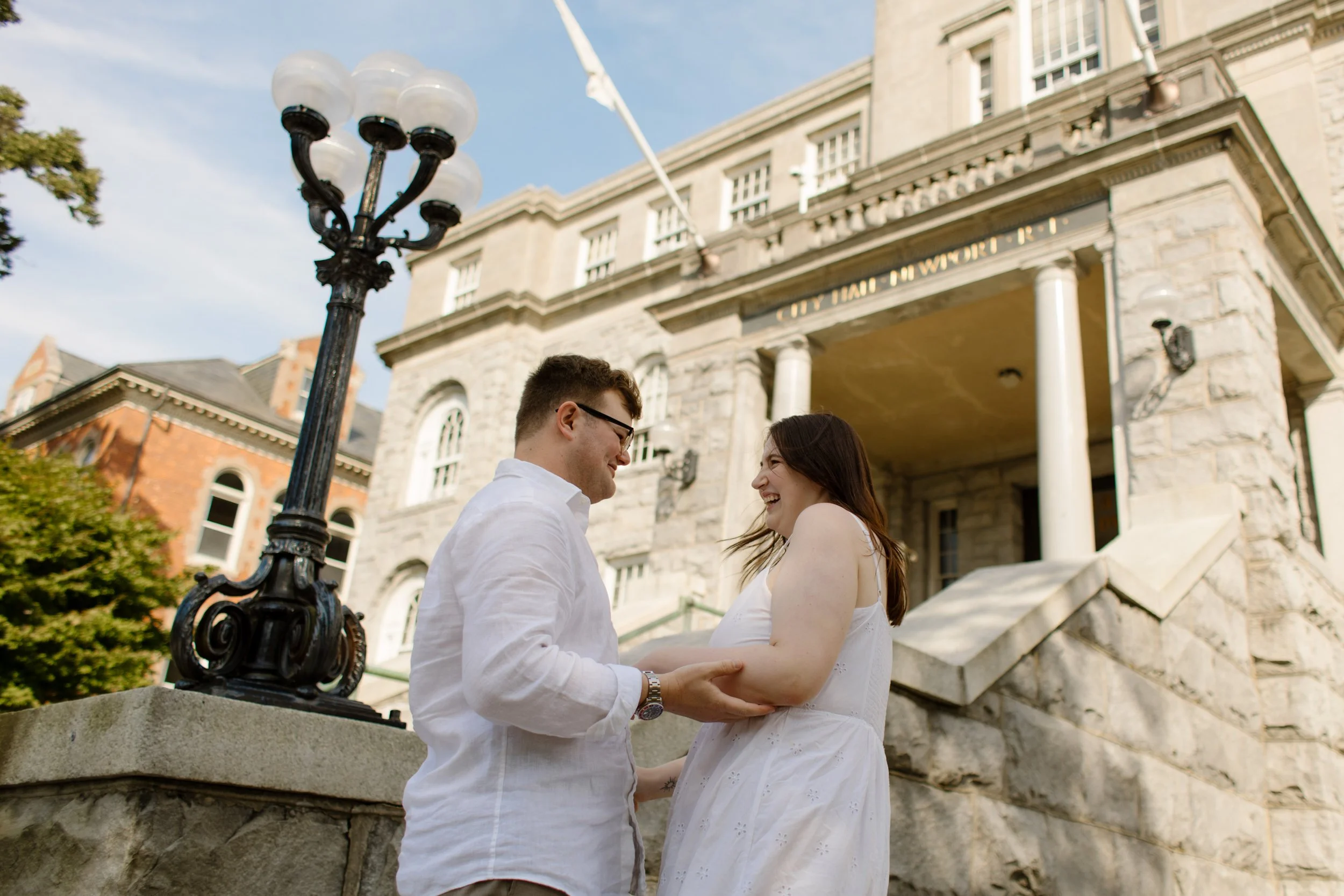 Couple laughing together outside Newport City Hall during Newport Rhode Island engagement photos