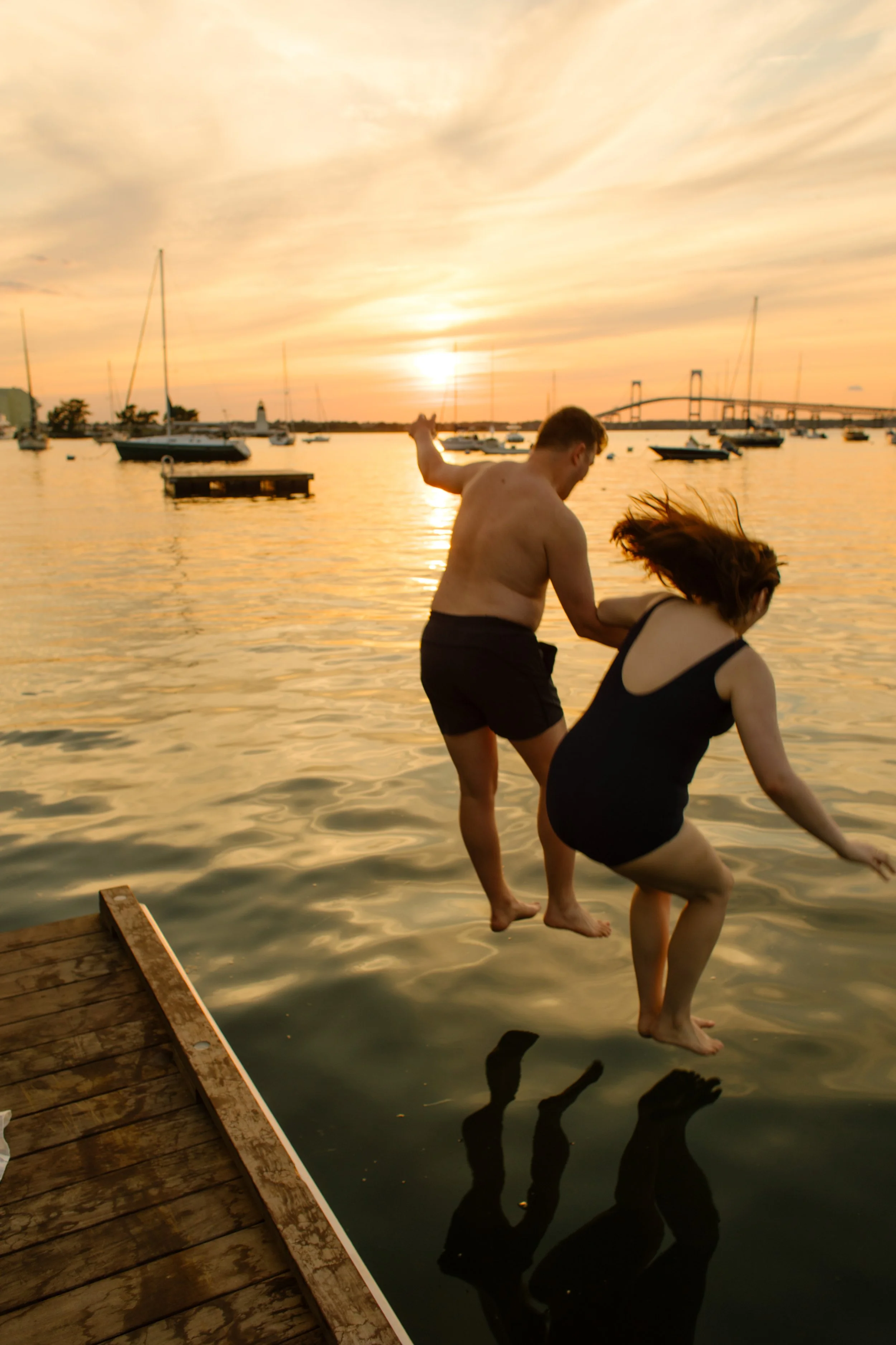 Couple splashing into water during Newport Rhode Island engagement photos at sunset