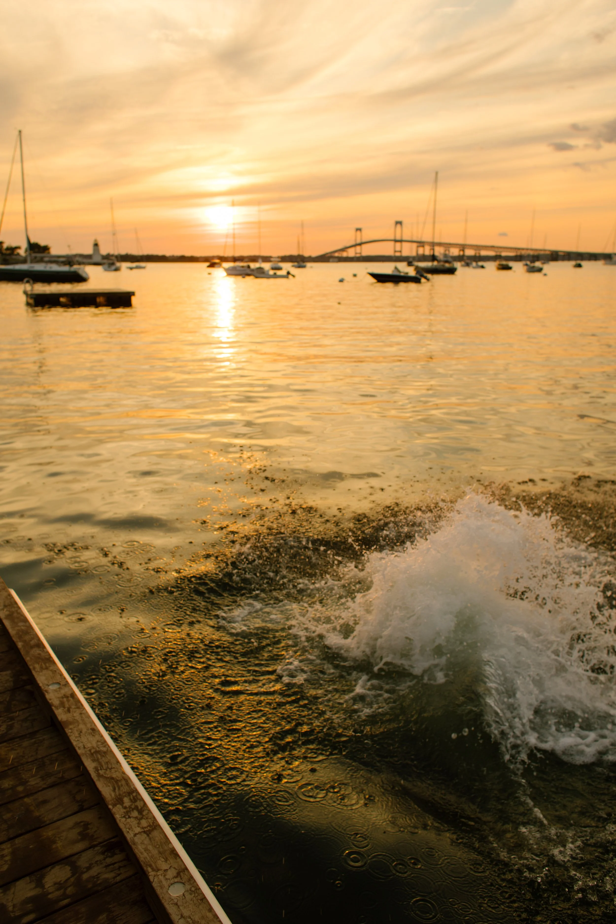 Couple splashing into water during Newport Rhode Island engagement photos at sunset