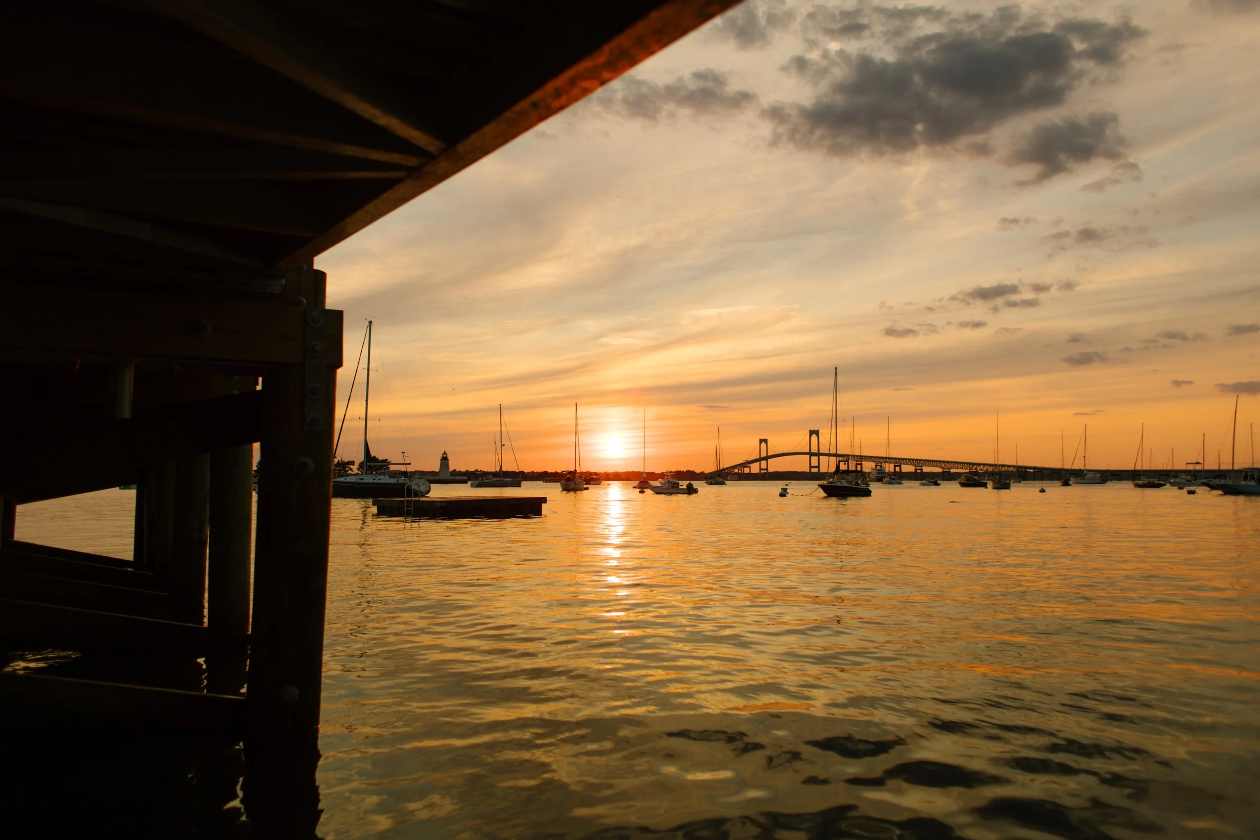 Golden sunset over Newport harbor with sailboats and Newport Bridge