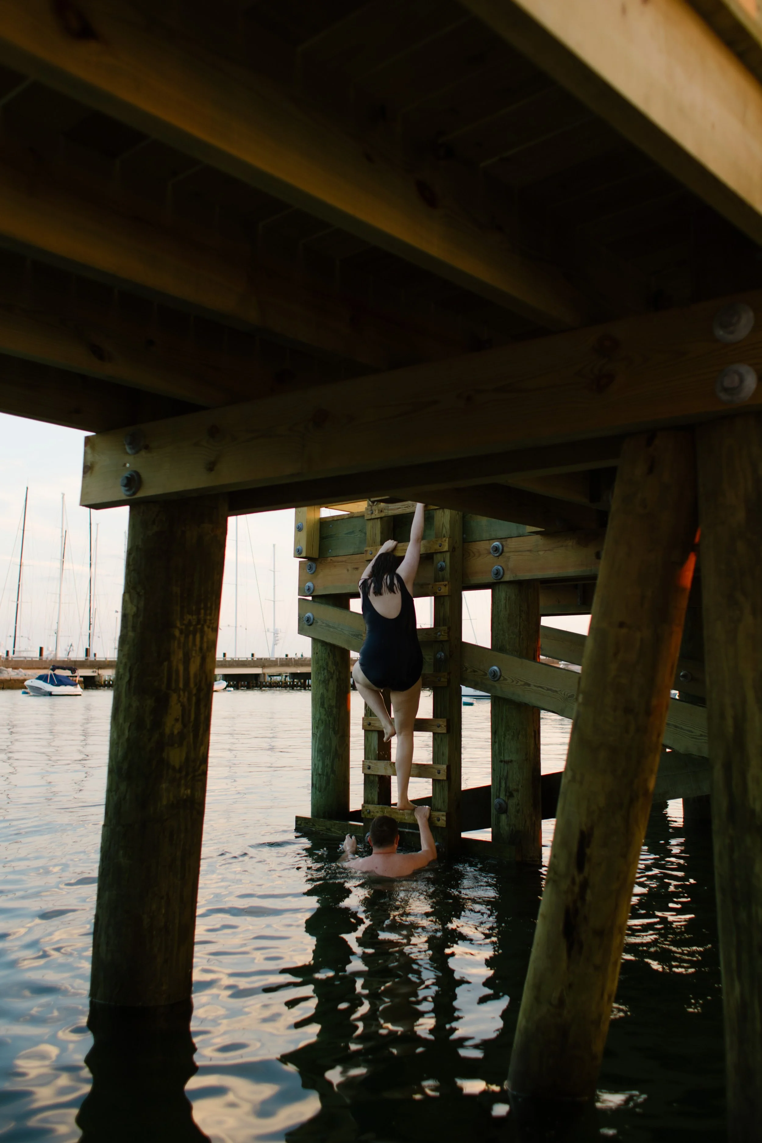 Couple climbing ladder under harbor dock after swimming during Newport Rhode Island engagement photos