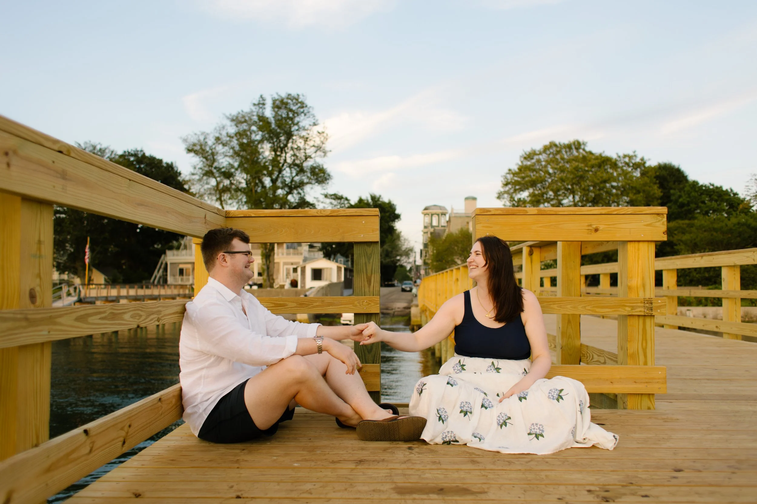 Couple sitting on wooden dock holding hands during Newport Rhode Island engagement photos