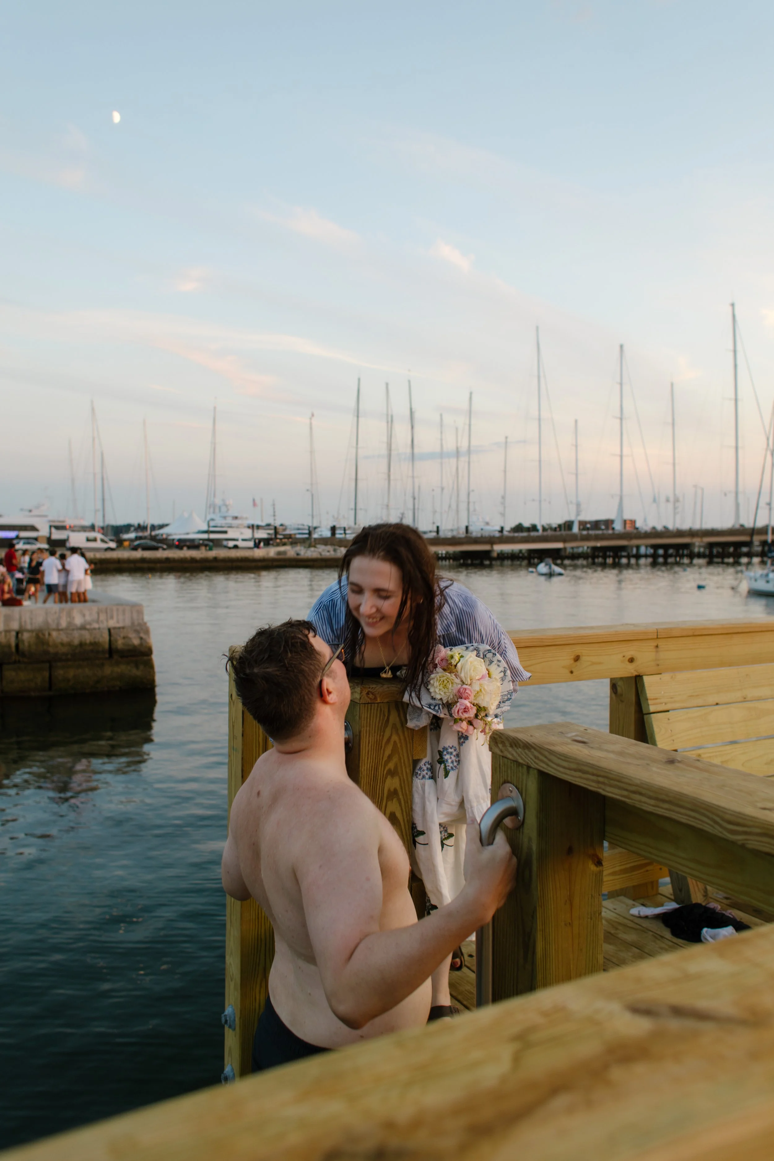 Couple smiling together on harbor dock after sunset swim during Newport Rhode Island engagement photos