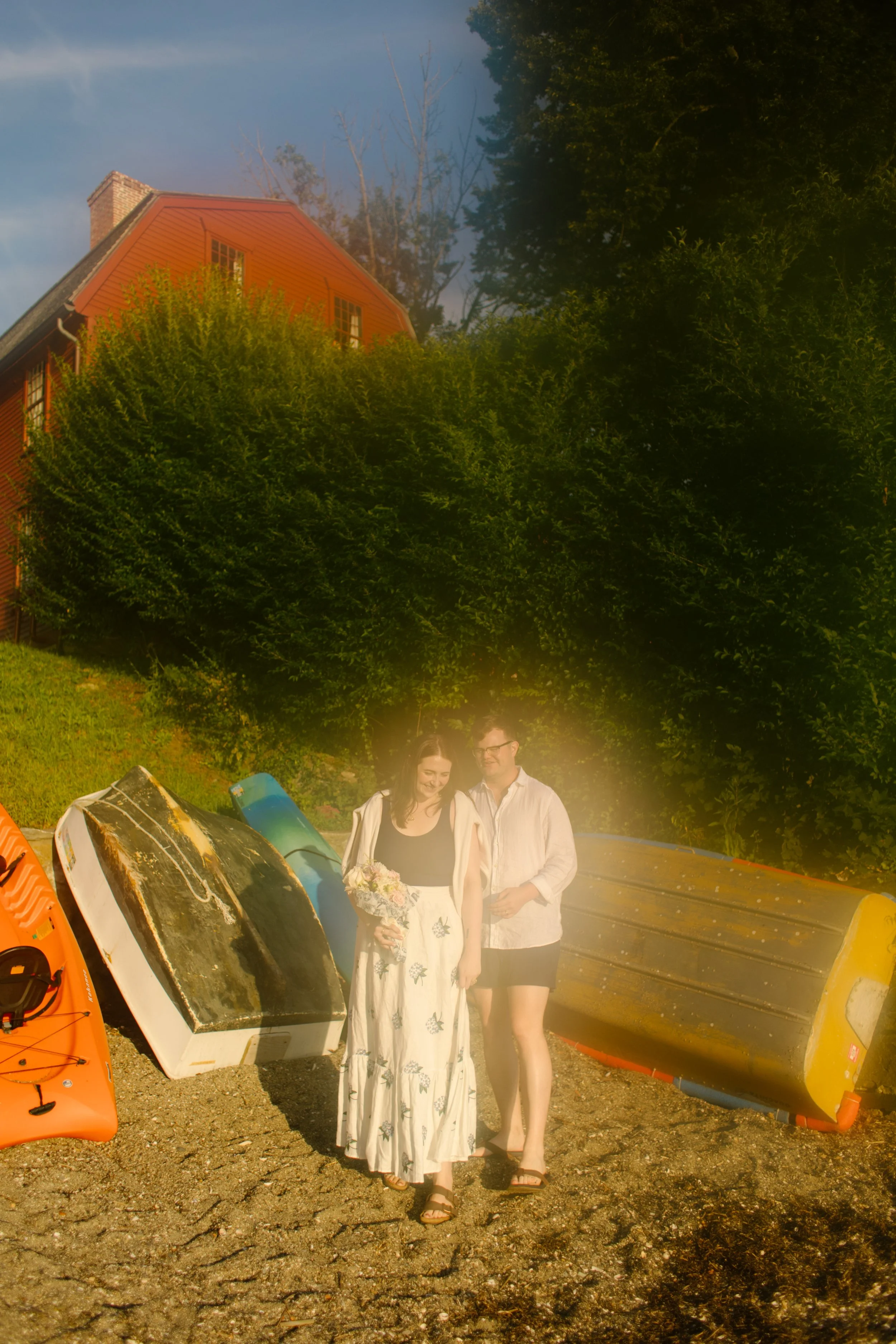 Couple standing beside colorful kayaks and boats during Newport Rhode Island engagement photos