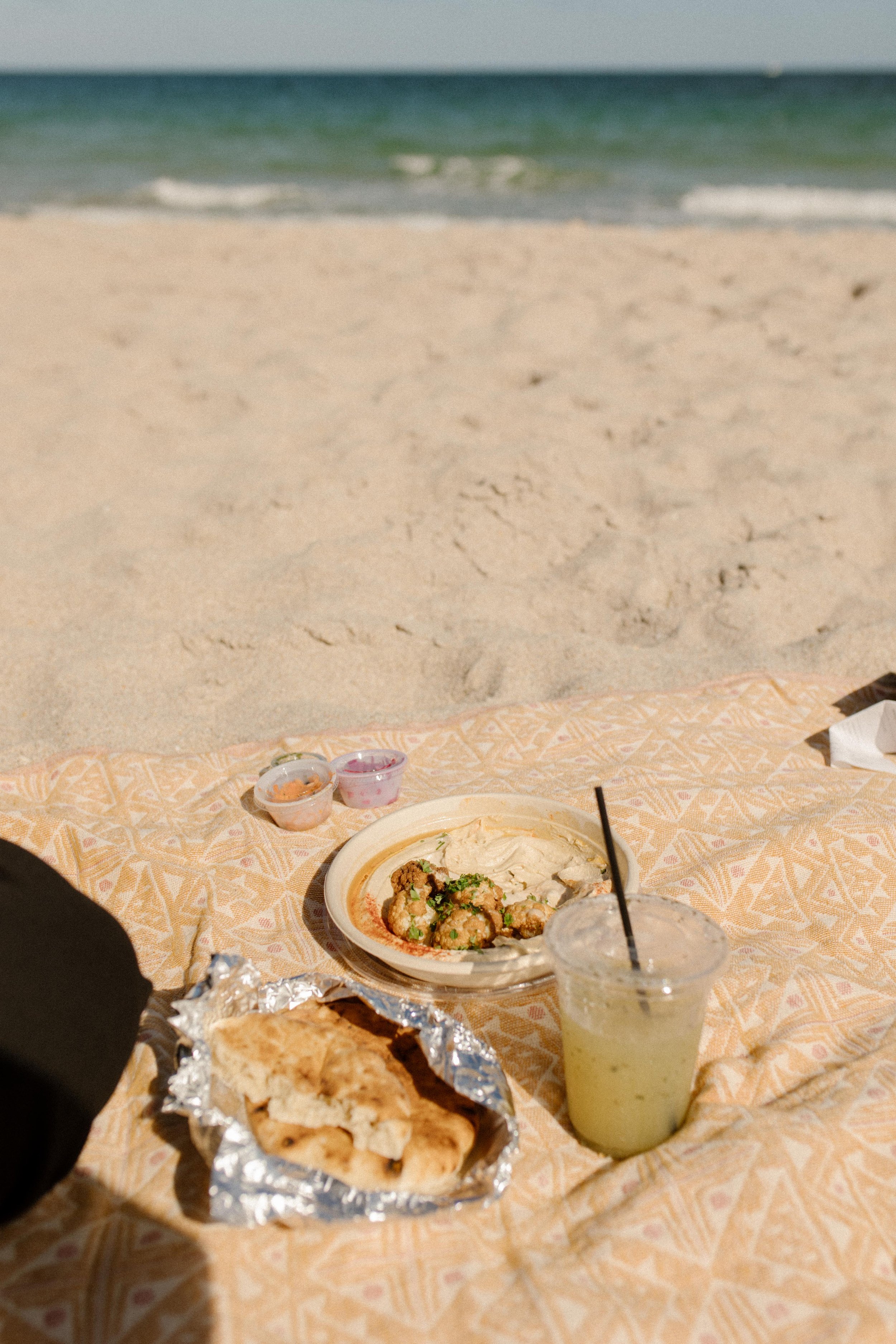 Beach picnic setup with hummus, pita, and drinks on a blanket in the sand, an intentional and relaxed detail that feels straight out of how to plan a surprise proposal by the ocean