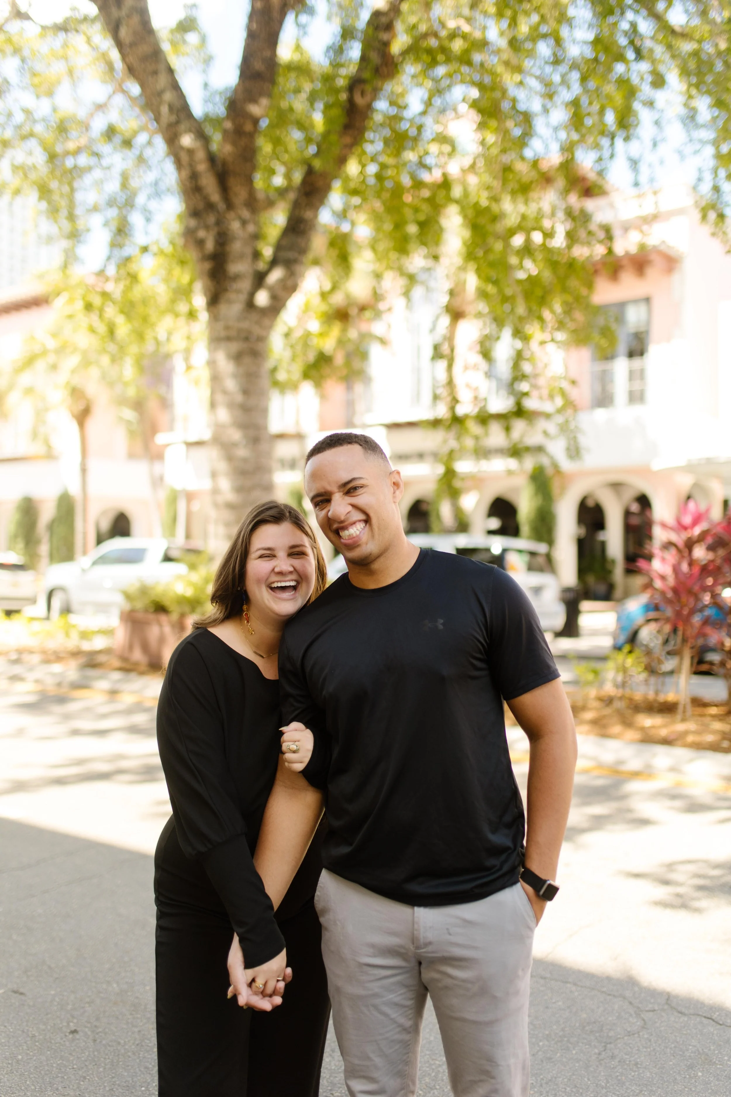 Couple standing close together on a quiet street, laughing and leaning into each other in a candid, joy-filled moment