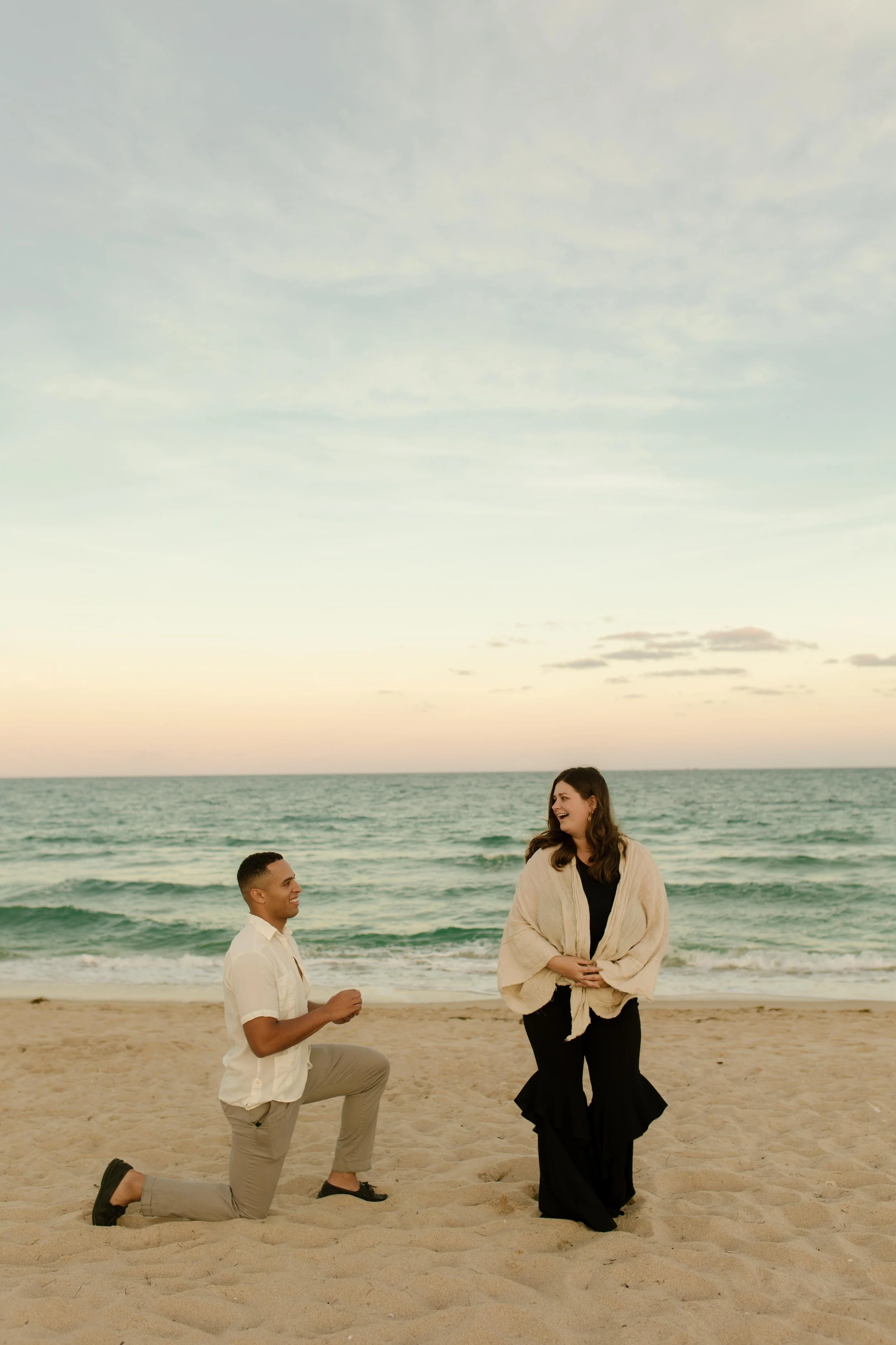 Man on one knee smiling up at his partner as she looks at him in disbelief, the quiet, electric pause that defines how to plan a surprise proposal