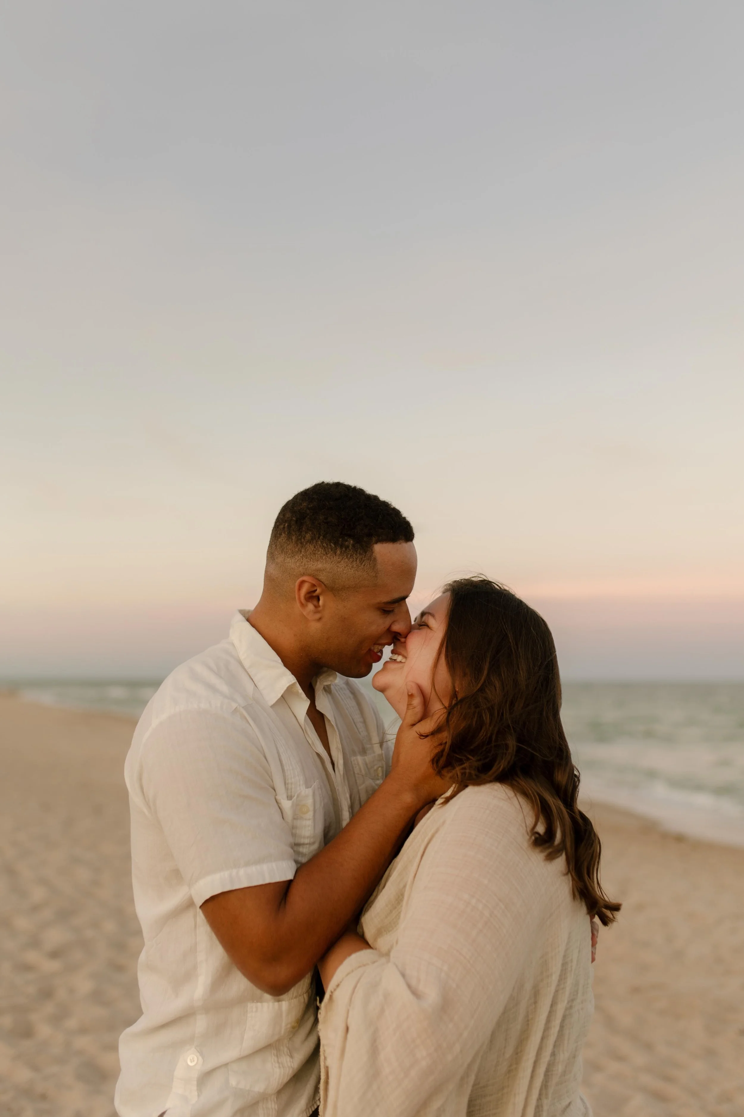Man pulling his partner in close as they smile into a kiss on the beach, the kind of moment that reflects how to plan a surprise proposal that leads into pure, unfiltered joy