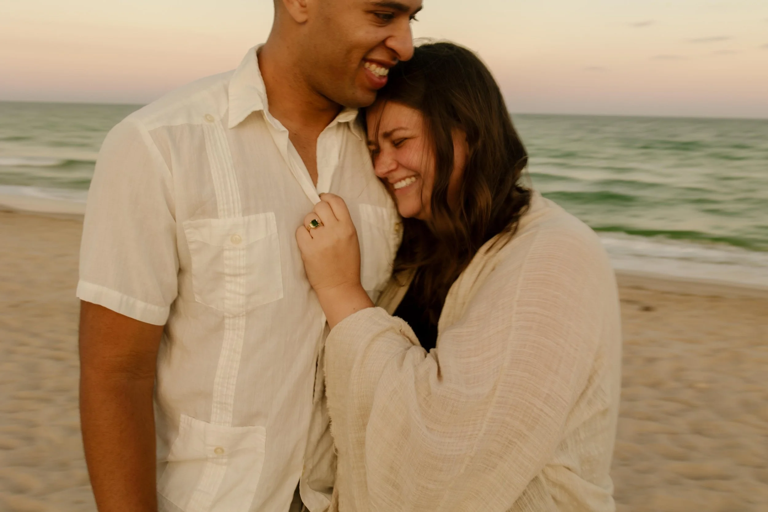 Close-up of a woman smiling into her partner’s chest with her hand resting over his heart, engagement ring visible and emotions still settling