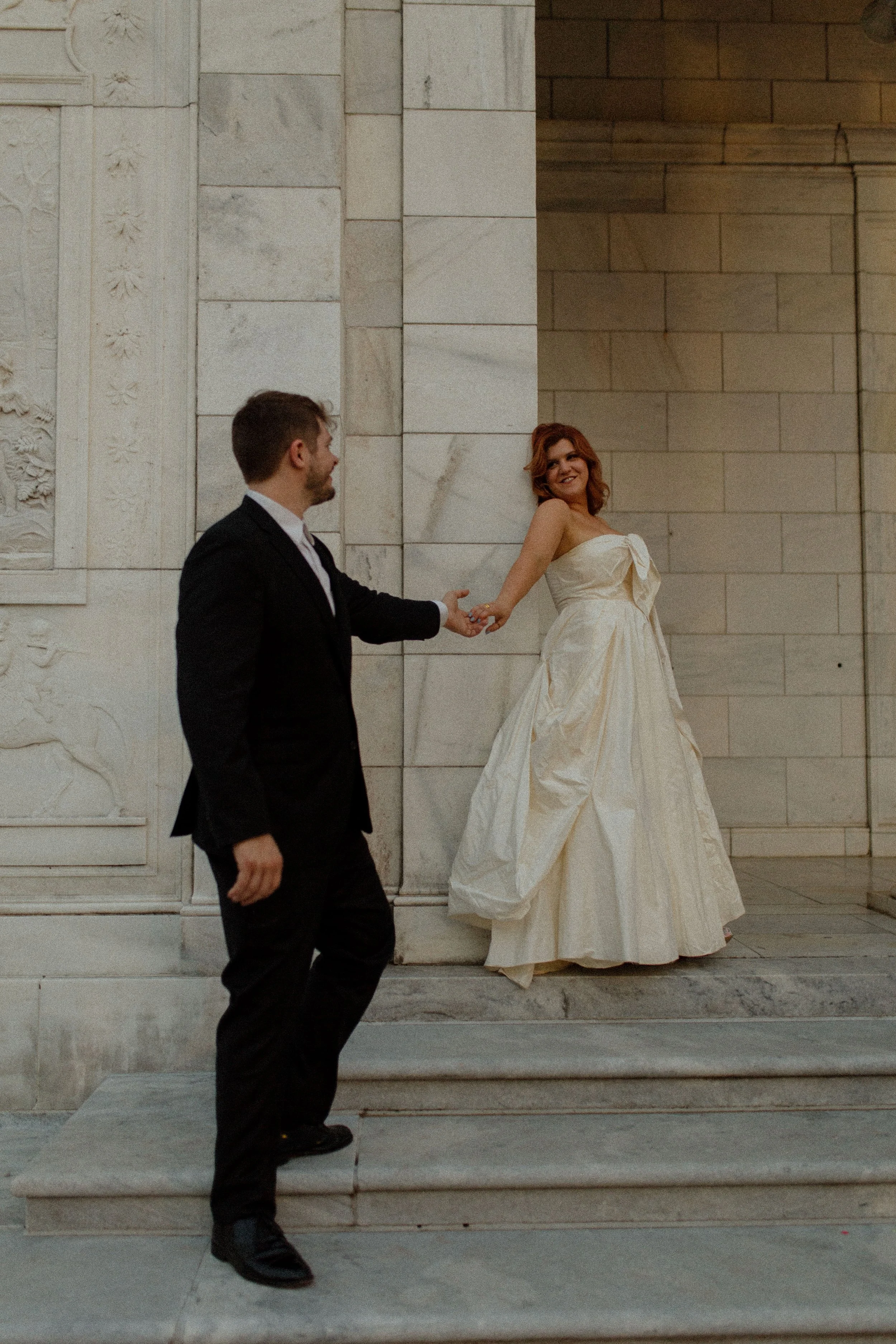 Groom gently leads bride by the hand as she steps up in her gown, smiling back at him in a playful and romantic pre wedding photos scene.