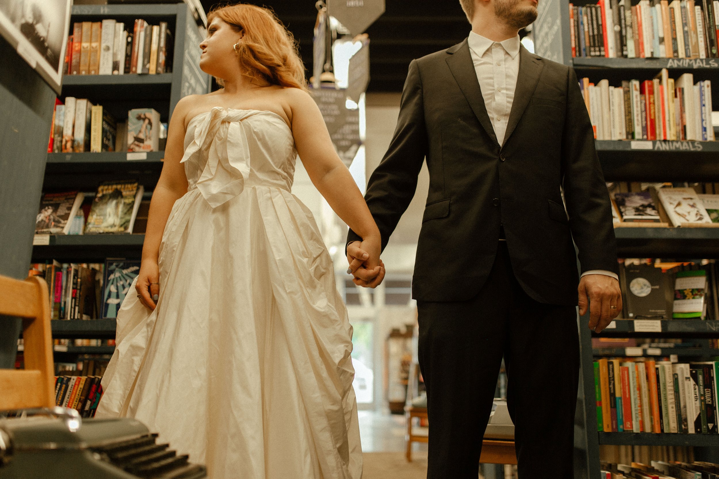 Bride and groom stand back to back holding hands, glancing in opposite directions in a playful and editorial pre wedding photos composition.