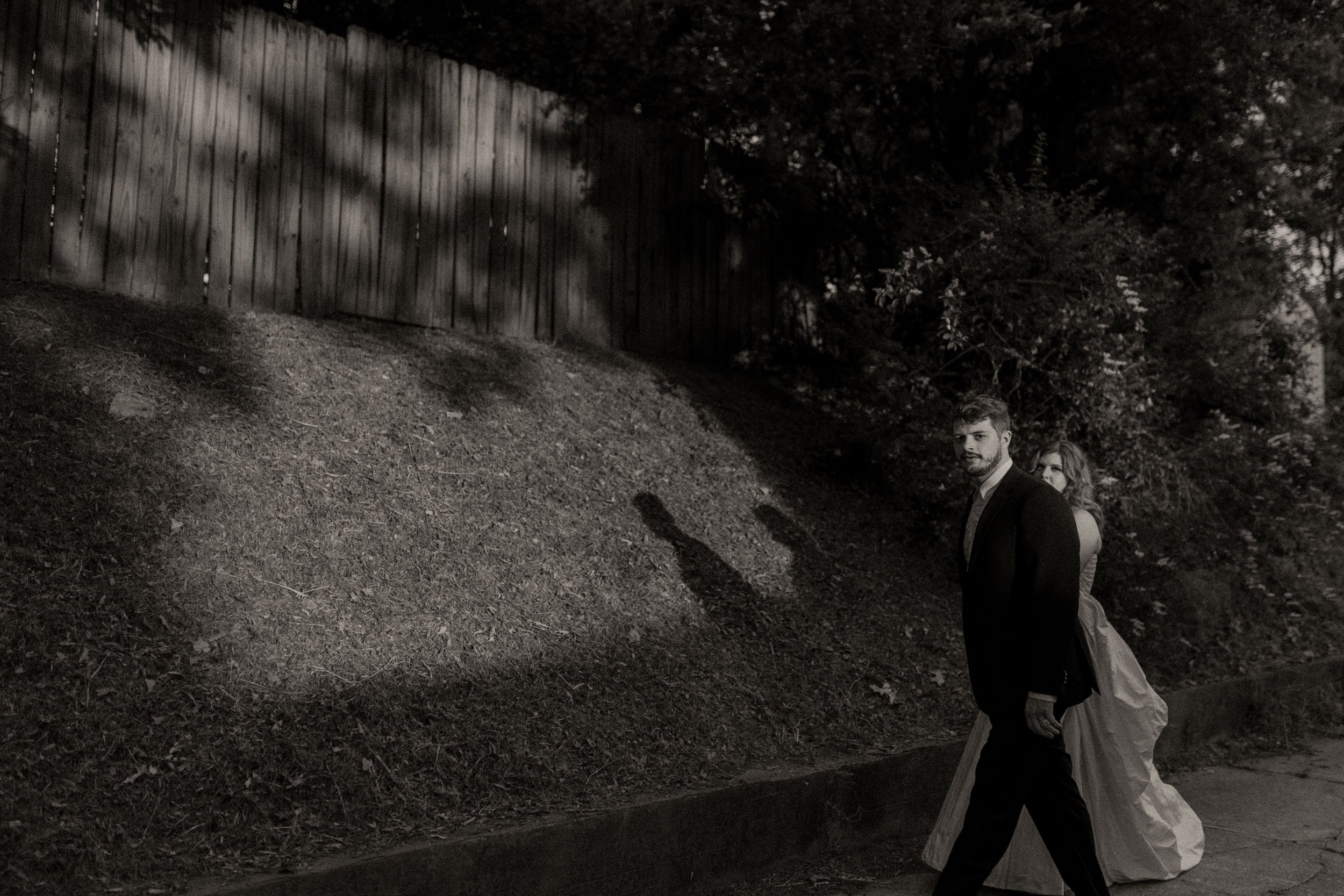Couple walks along a shadowed street, their silhouettes stretching across the wall in a moody black and white pre wedding photos scene.