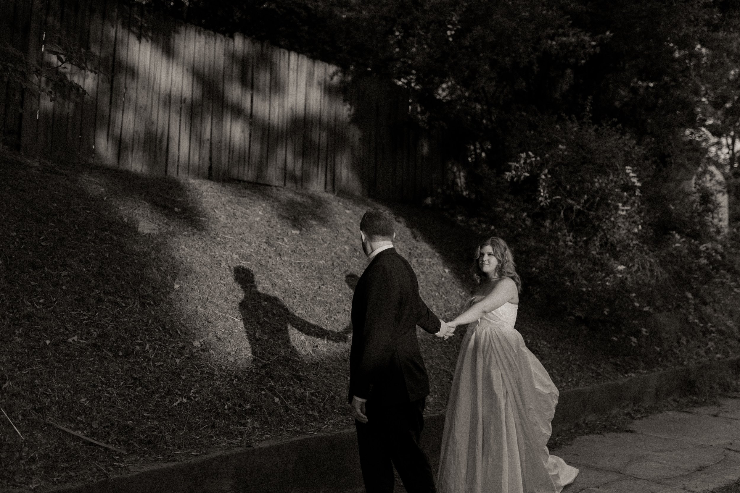 Bride reaches back to hold groom’s hand as they walk, their shadows mirroring the moment in a cinematic pre wedding photos frame.