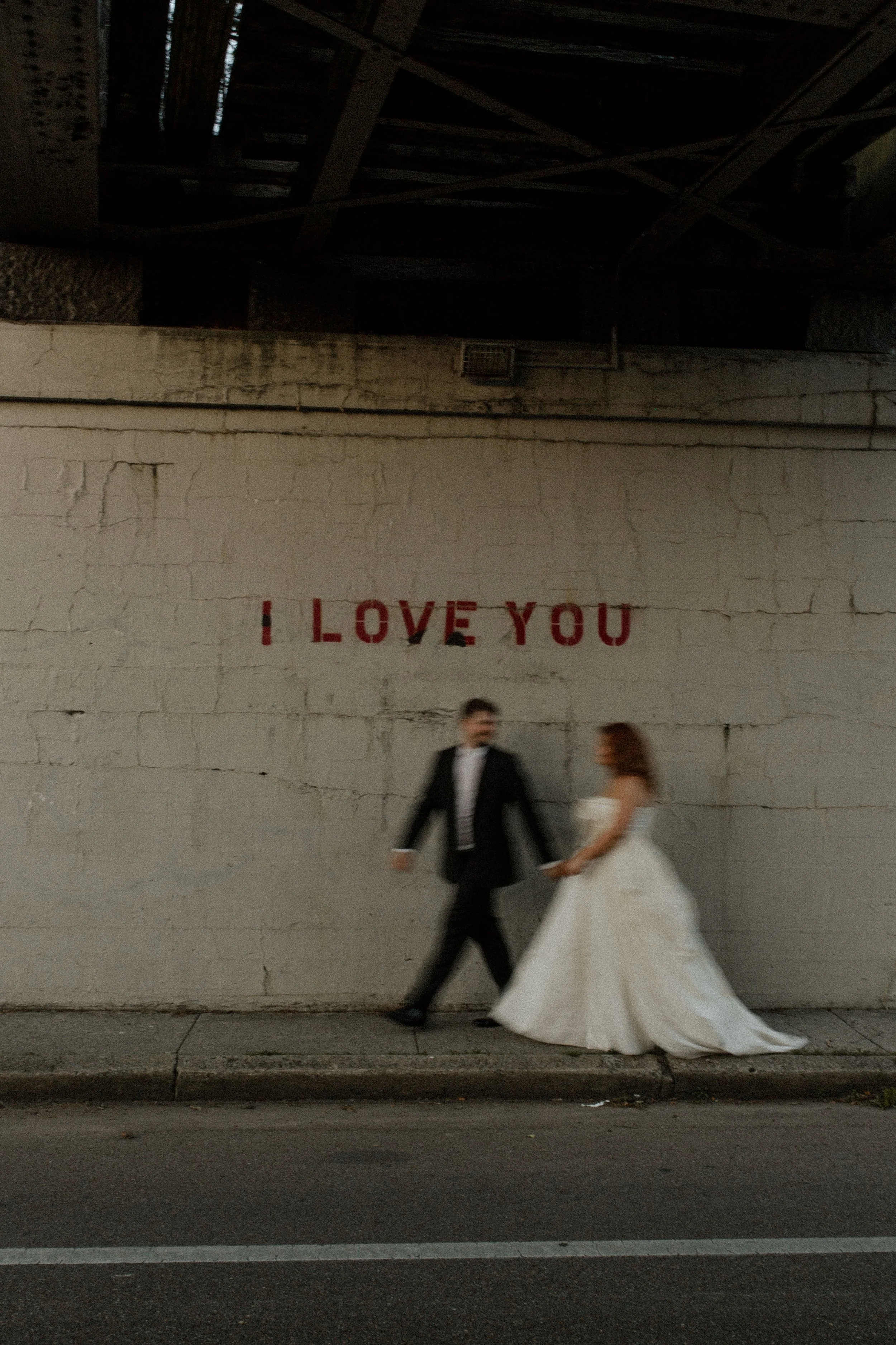 Motion-blurred couple walks hand in hand past a wall painted with “I love you,” creating an artistic and storytelling-driven pre wedding photos moment.