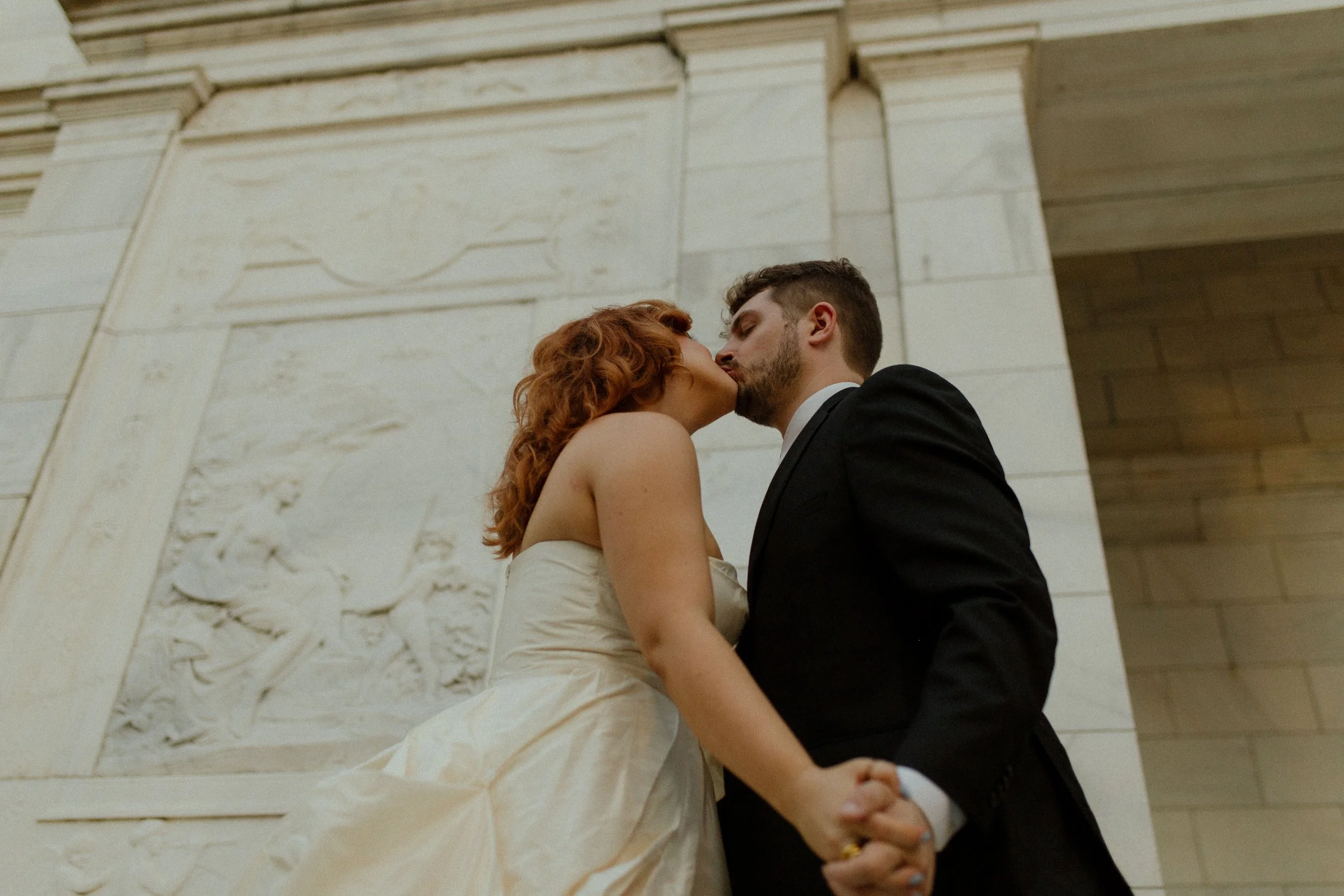 Low angle of the couple kissing while holding hands, the bride’s dress catching movement in a dramatic pre wedding photos frame.