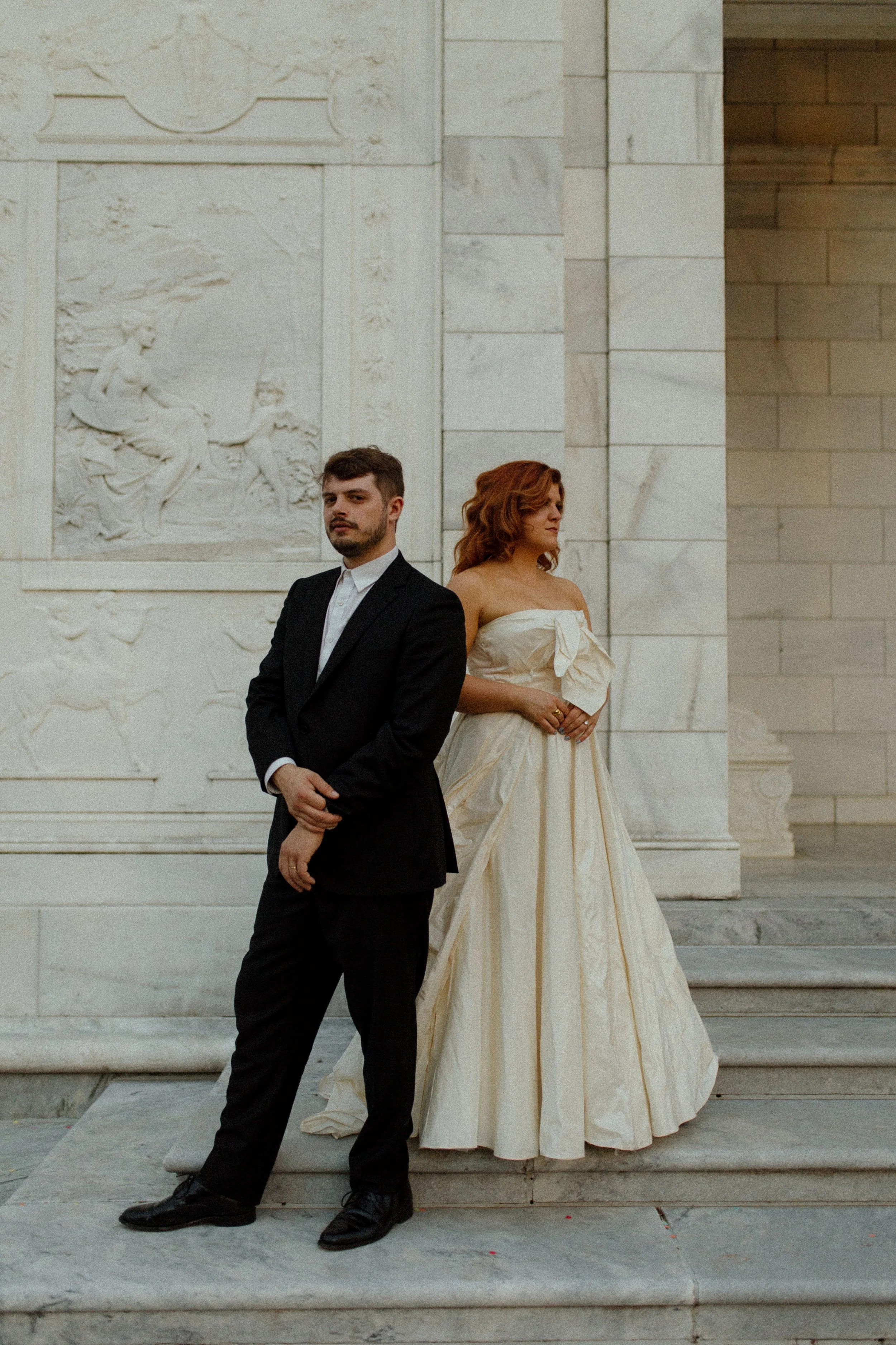 Bride and groom stand back to back against a stone wall, both gazing off in opposite directions in an editorial and timeless pre wedding photos scene.