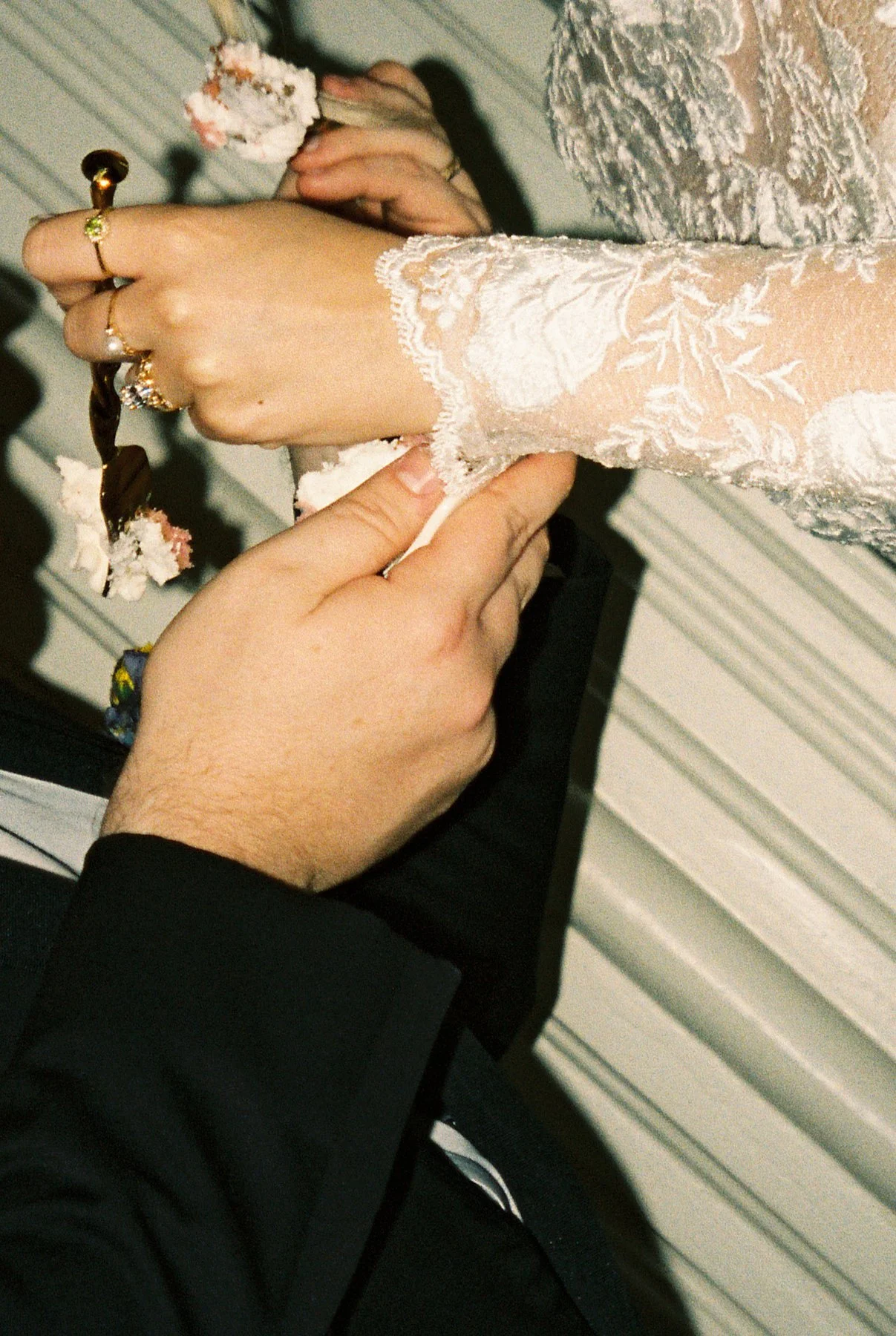 close-up of bride and groom feeding each other cake, lace sleeves and frosting-covered hands capturing a playful, intimate wedding moment