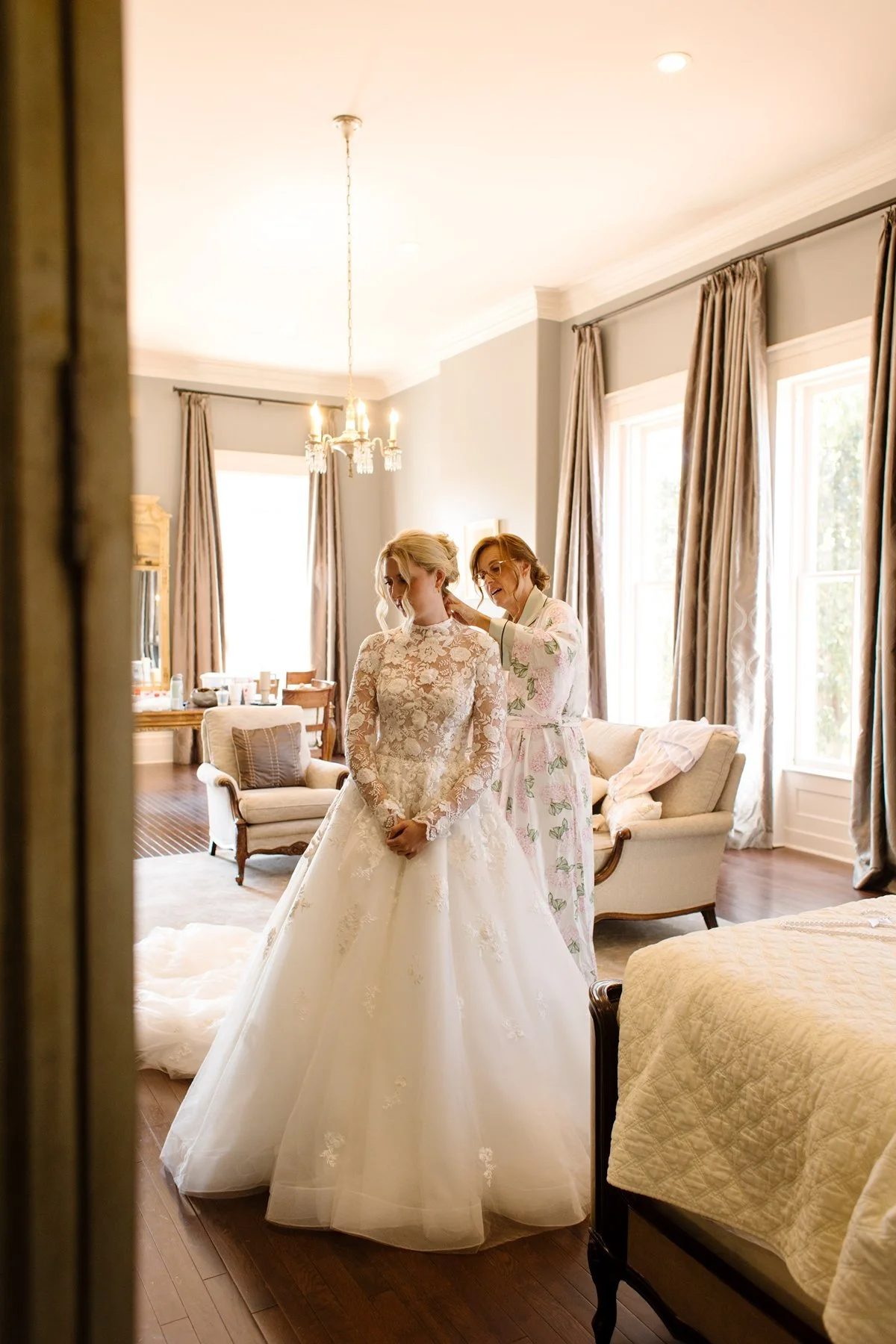 bride getting ready with her mother in a light-filled room, buttoning delicate lace dress in a timeless memphis wedding venue suite