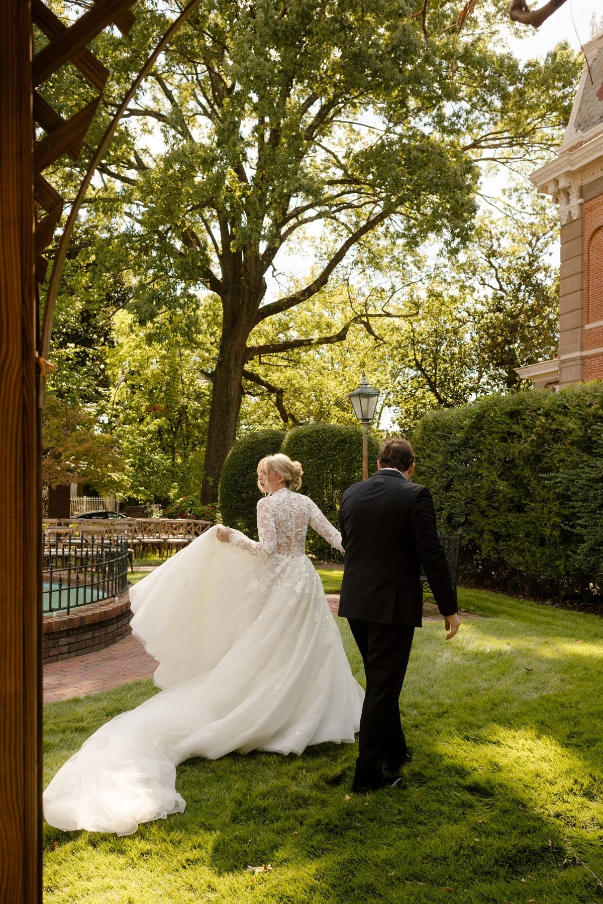 bride and groom walking hand in hand through garden lawn with sweeping veil trailing behind at an elegant memphis wedding venue