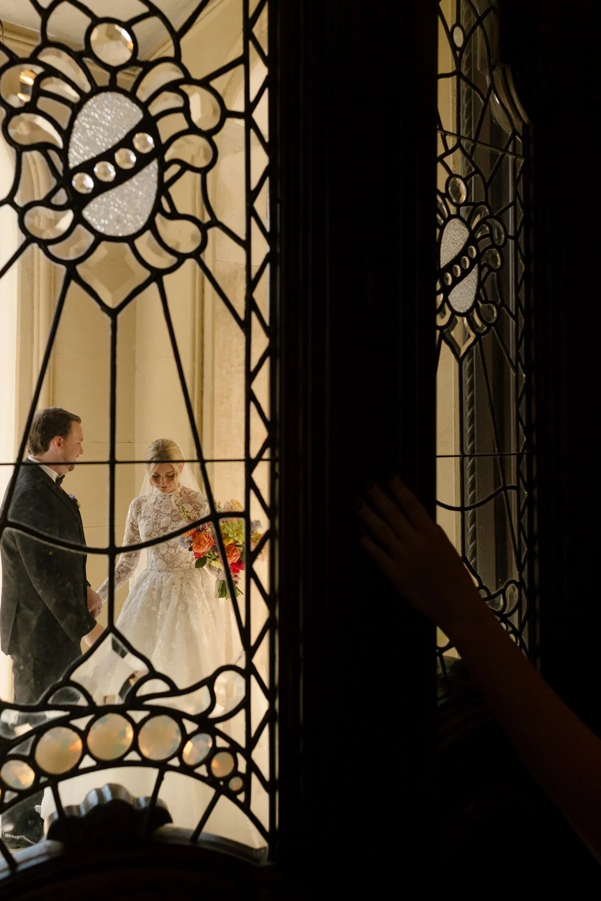 ceremony moment framed through ornate stained glass doors, bride and groom holding hands inside a historic memphis wedding venue