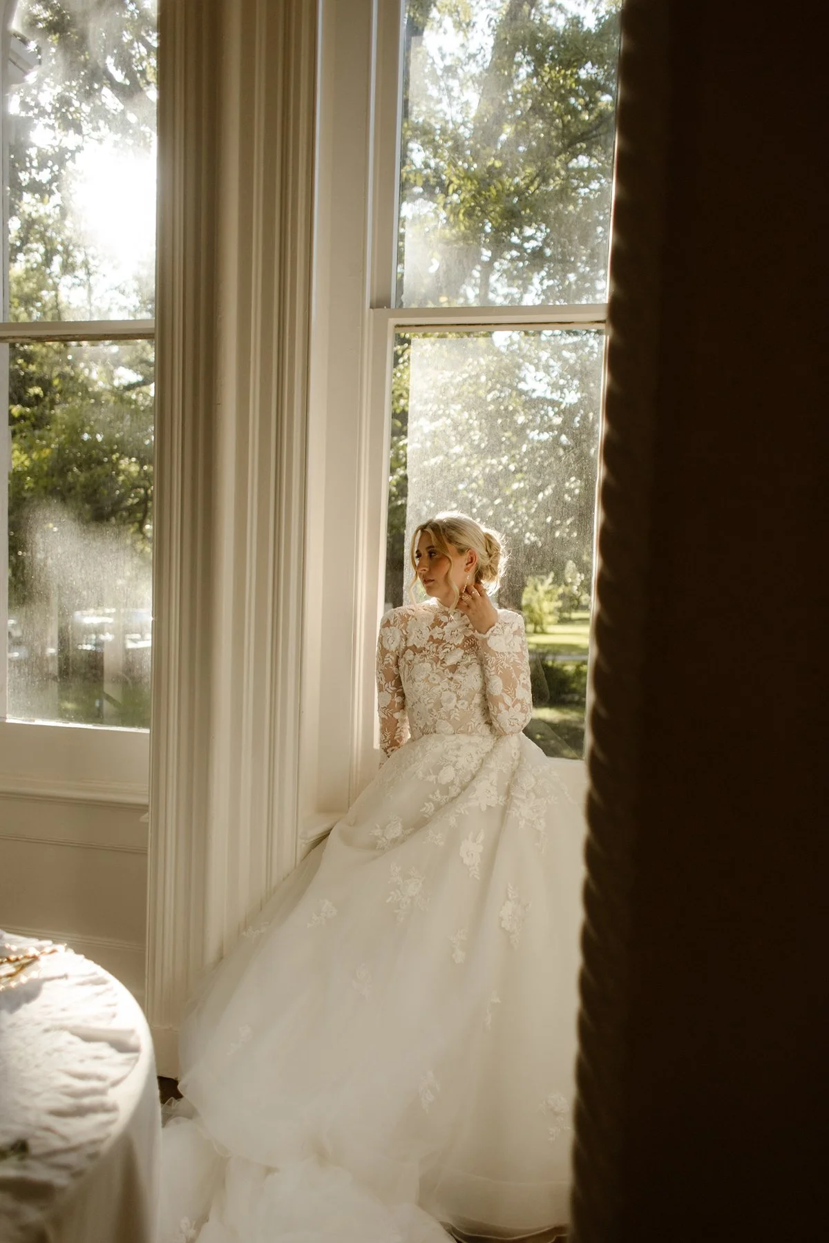 bride sitting by tall windows in soft morning light, adjusting earrings in a quiet pre-ceremony moment inside a memphis wedding venue