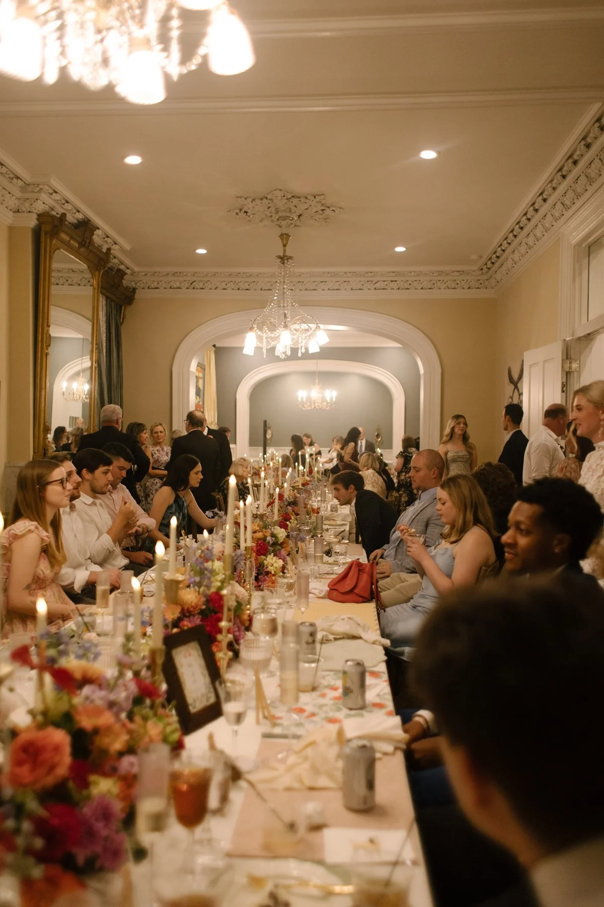 long reception table filled with candles, florals, and guests gathered in a warm, intimate dining room celebration