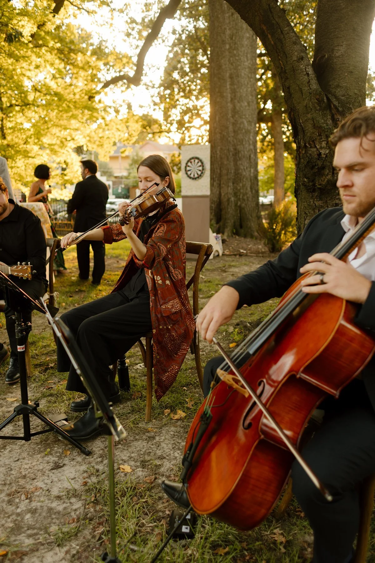 string quartet playing during an outdoor ceremony under tall trees at a memphis wedding venue, warm golden light filtering through leaves as guests gather