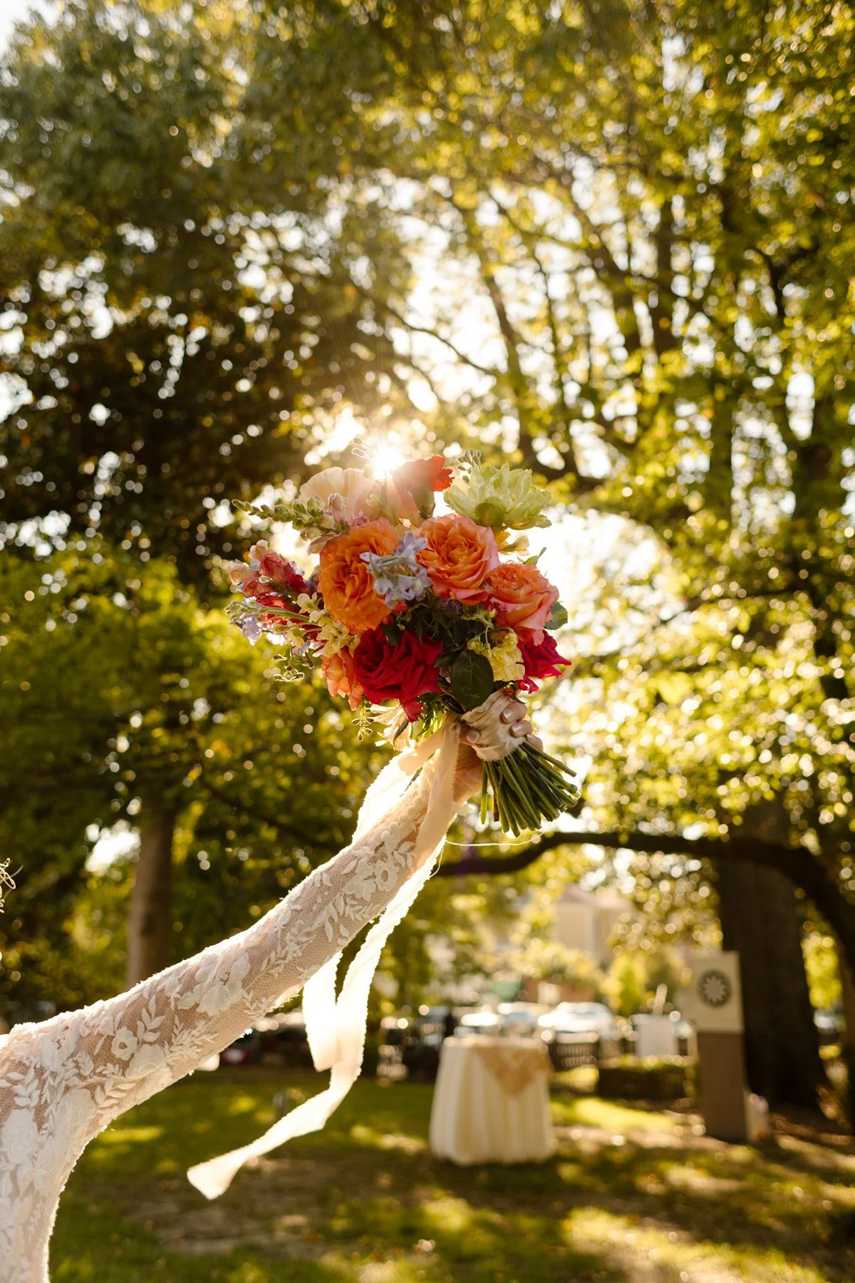 bride holding vibrant bouquet up to the sun, light streaming through trees during golden hour at an outdoor memphis wedding venue