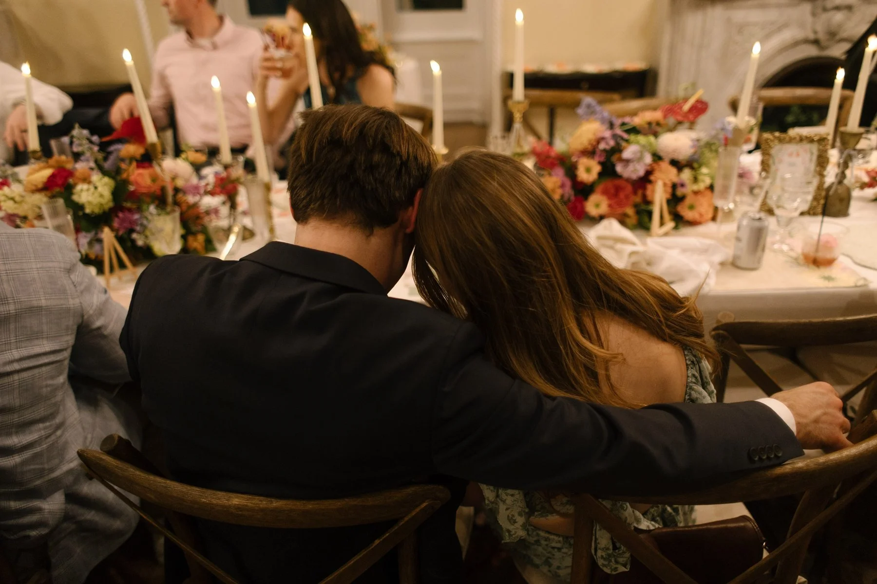 couple leaning into each other at reception table surrounded by candles and colorful florals, a quiet pause in the middle of celebration