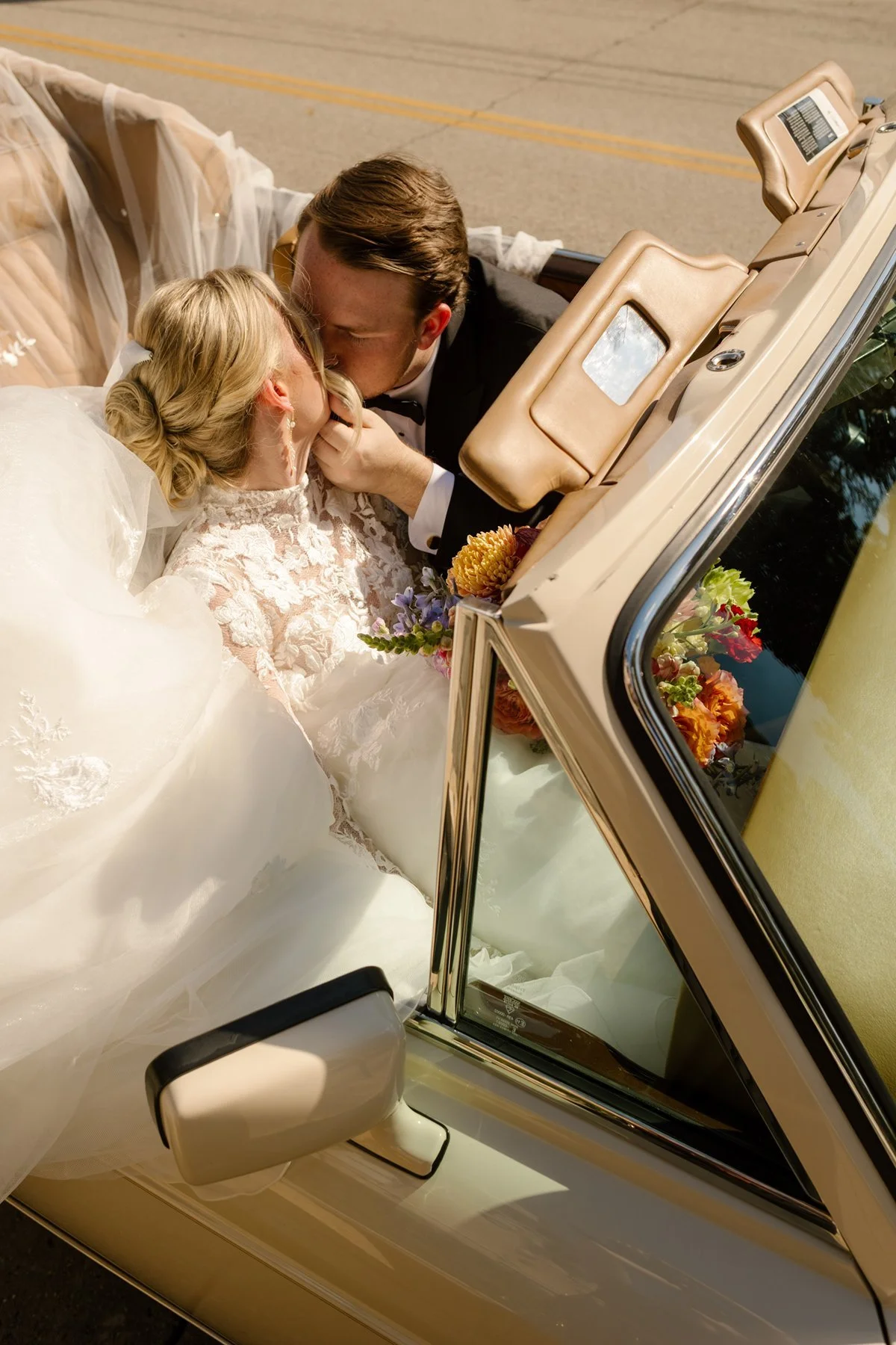 bride and groom kissing in convertible, veil and dress spilling over the car in a cinematic just-married moment