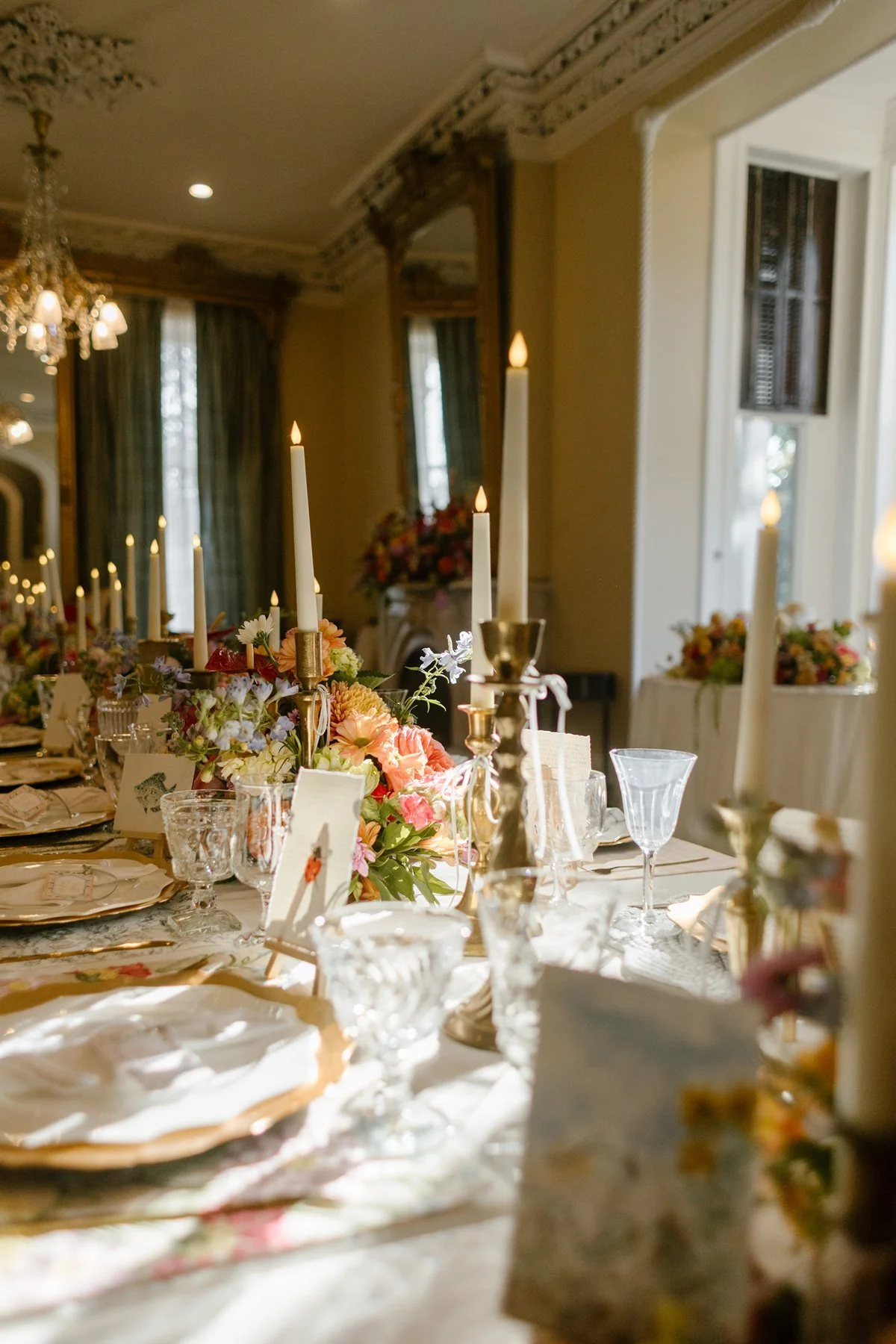 Long reception table set with candles, glassware, and vibrant floral arrangements glowing in warm, golden light.