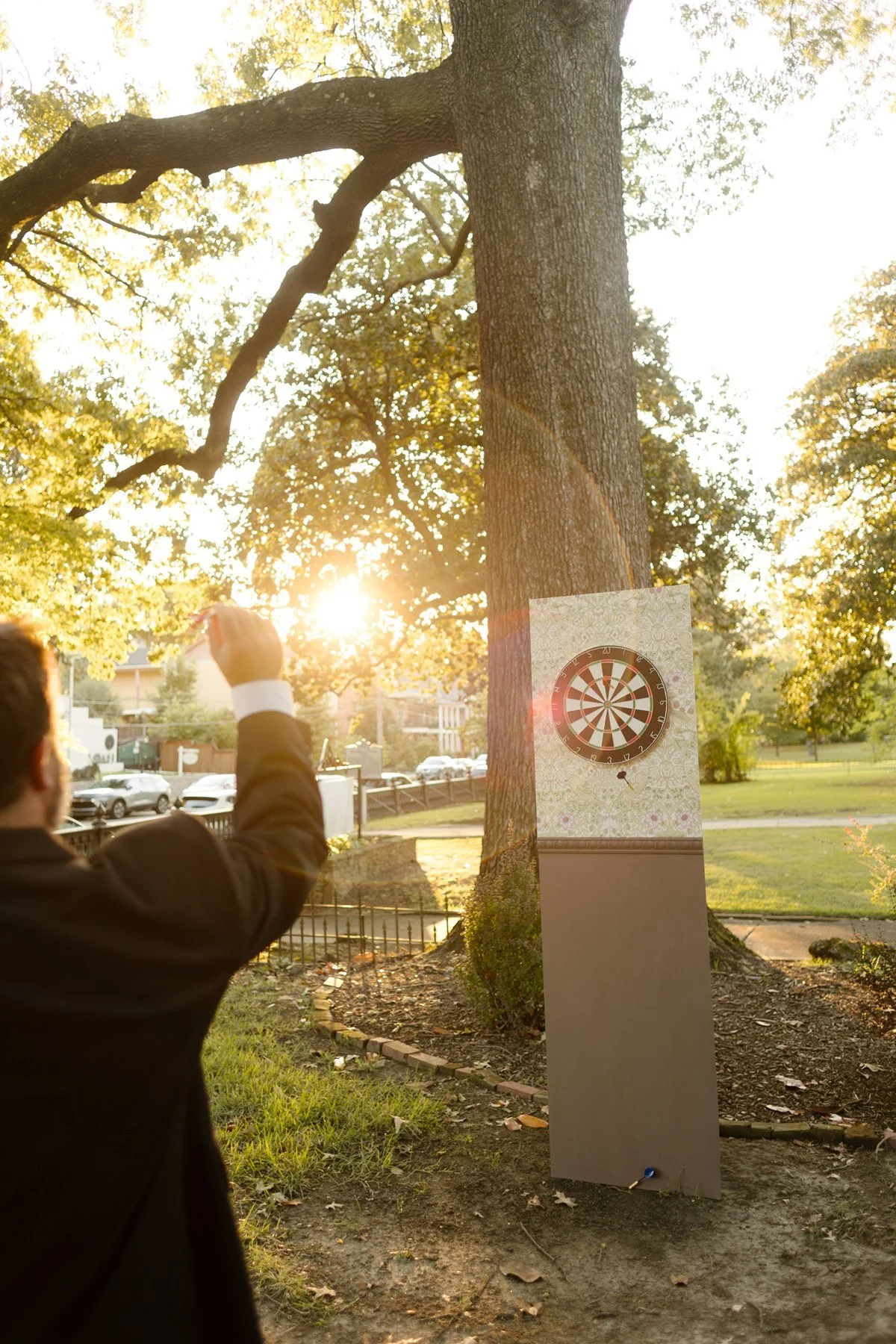 Guest throwing a dart at a board set up on a tree during golden hour, sunlight streaming through the branches.