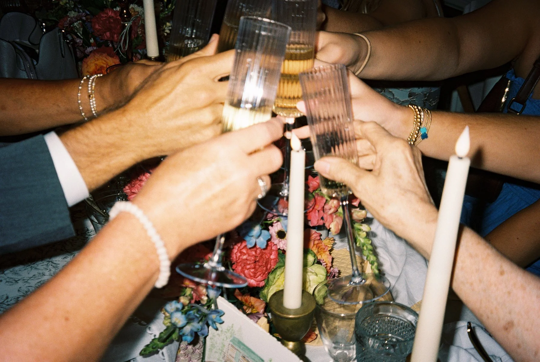 Guests clinking champagne glasses in a celebratory toast over a candlelit table filled with florals.