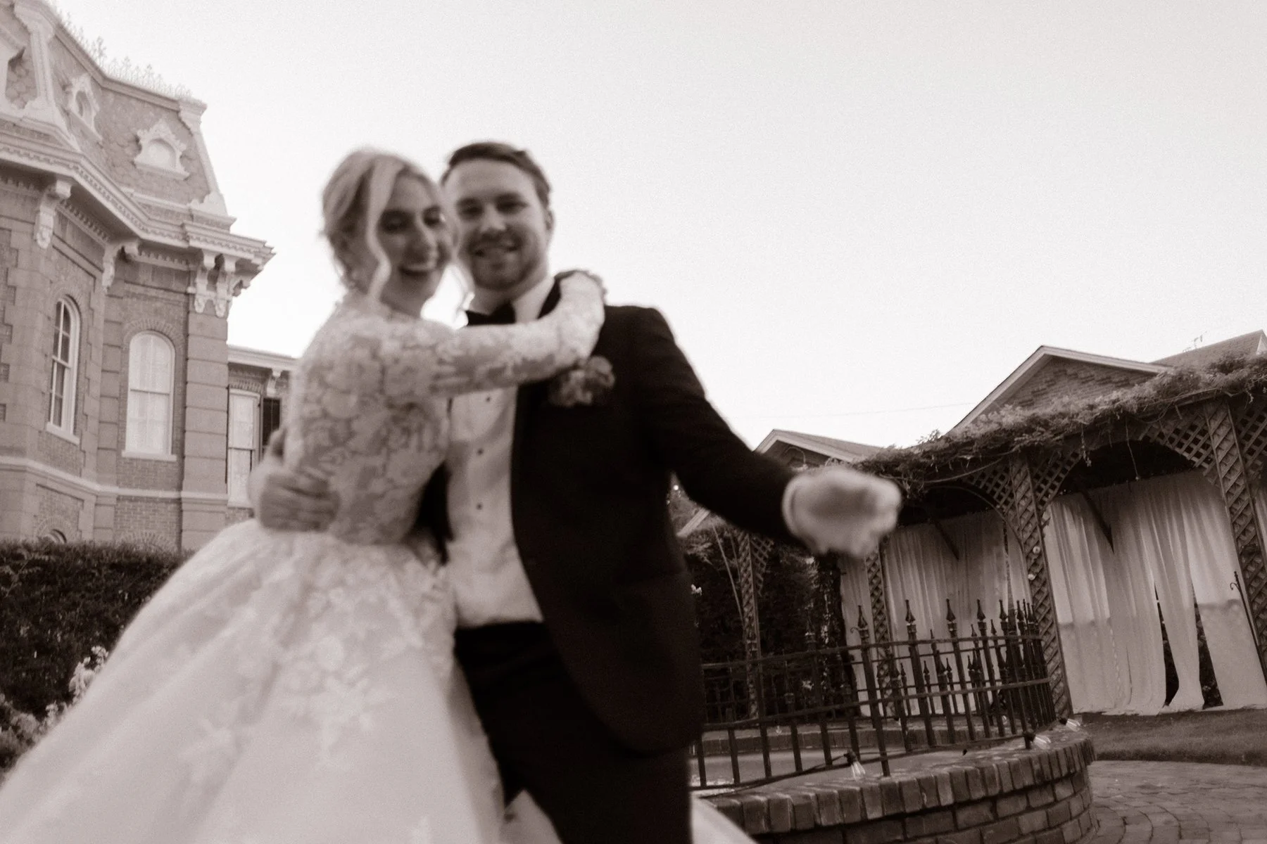 Blurry black-and-white photo of the bride and groom laughing and holding each other close outside the venue.