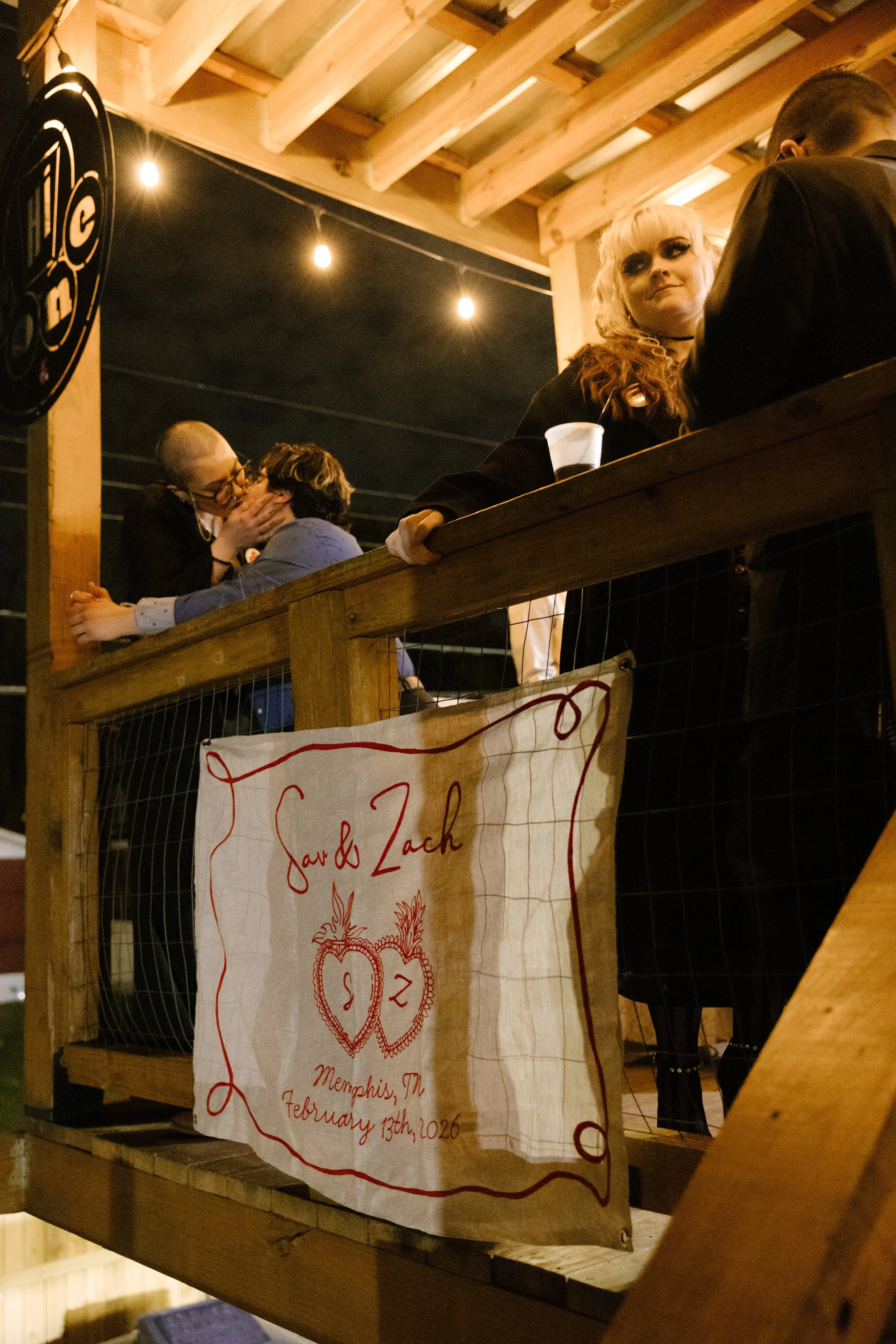 Couple kissing on a balcony at night above a handmade wedding banner in Memphis, capturing candid and unconventional wedding energy
