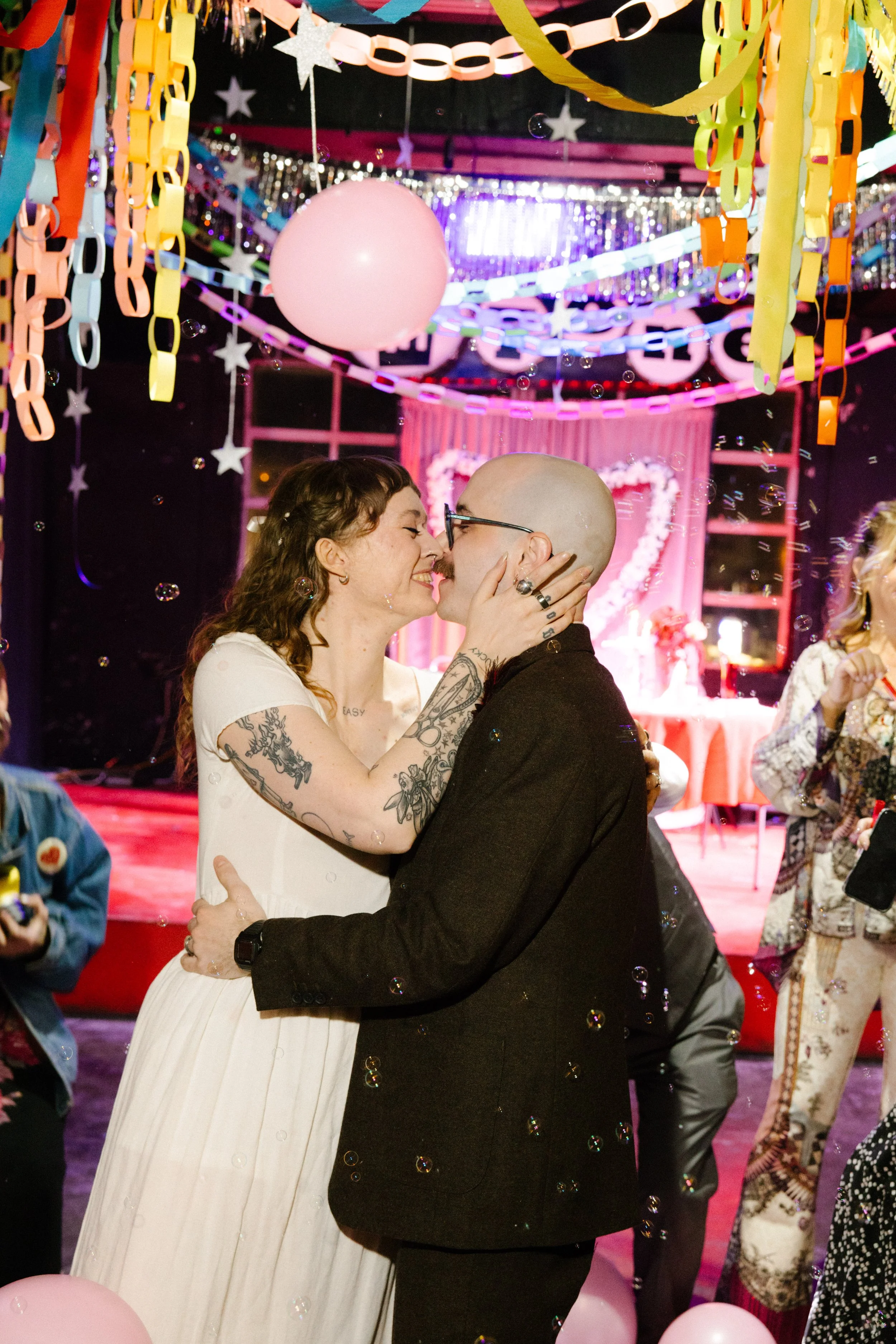 Couple kissing on the dance floor surrounded by balloons, bubbles, and colorful decor showcasing fun and immersive unique wedding ideas